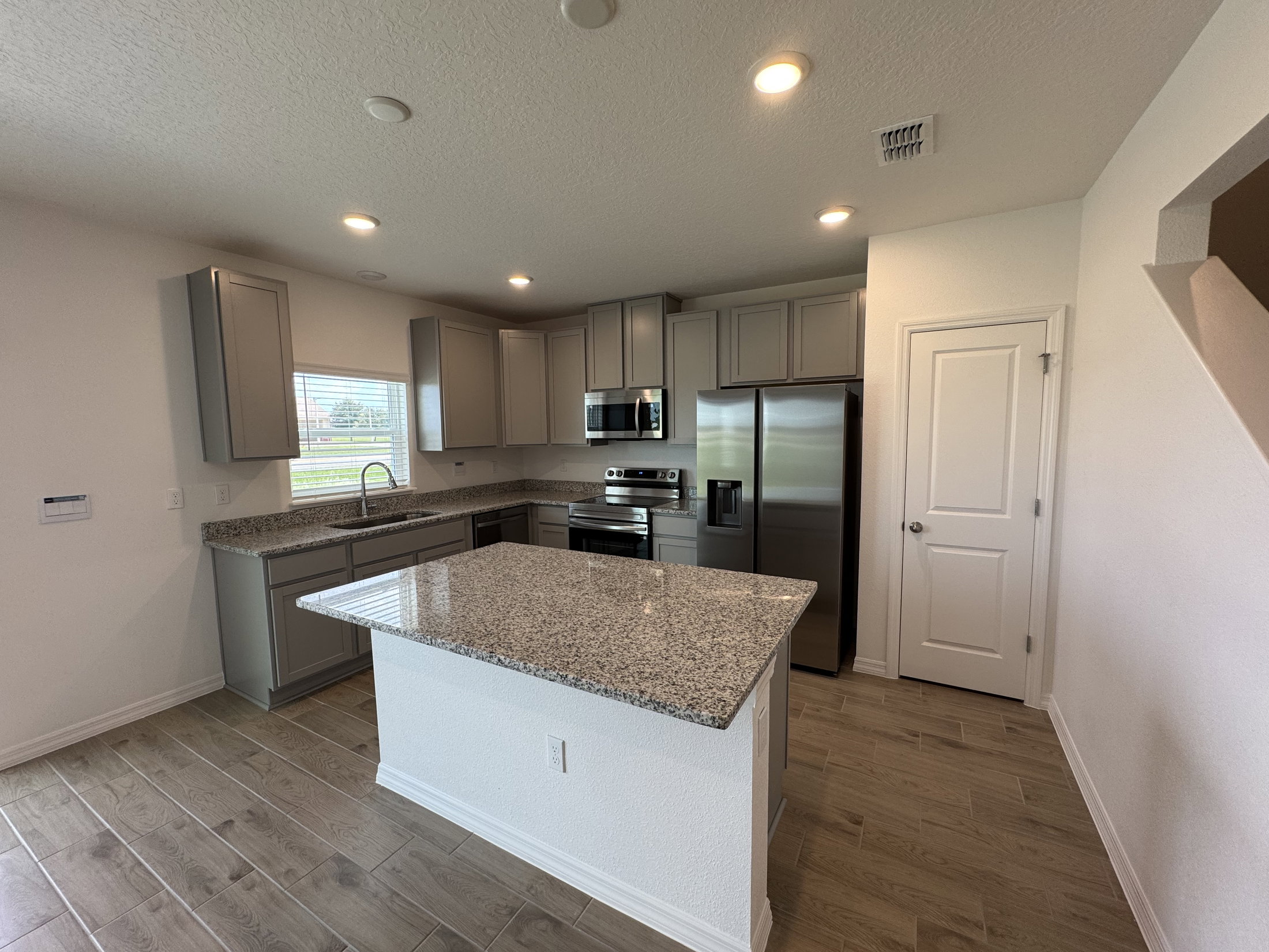 Modern kitchen featuring gray cabinetry, granite countertops, stainless steel appliances, and wood-like tile flooring.