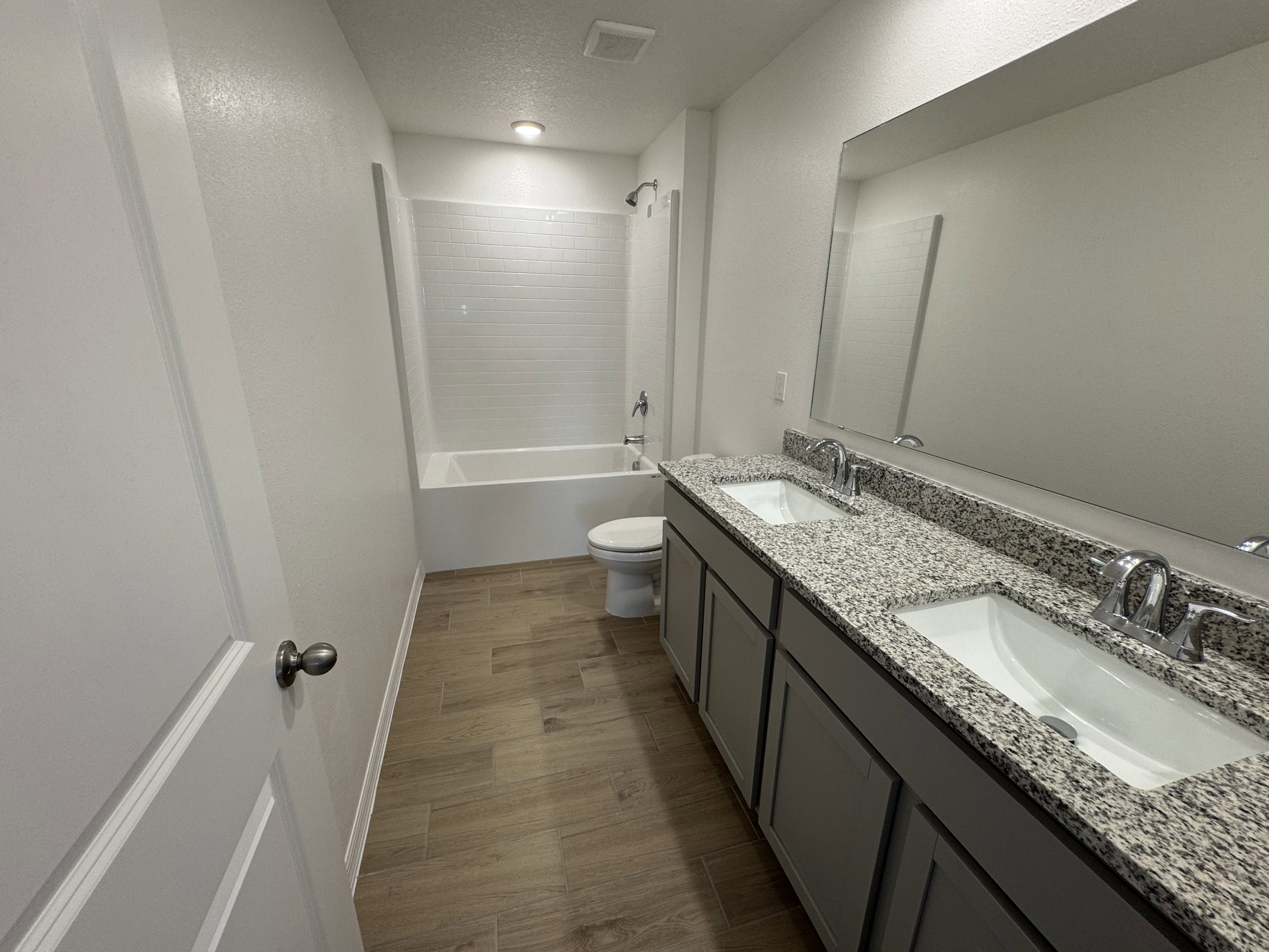 A modern bathroom featuring a double sink vanity, a large mirror, and a bathtub with a showerhead.