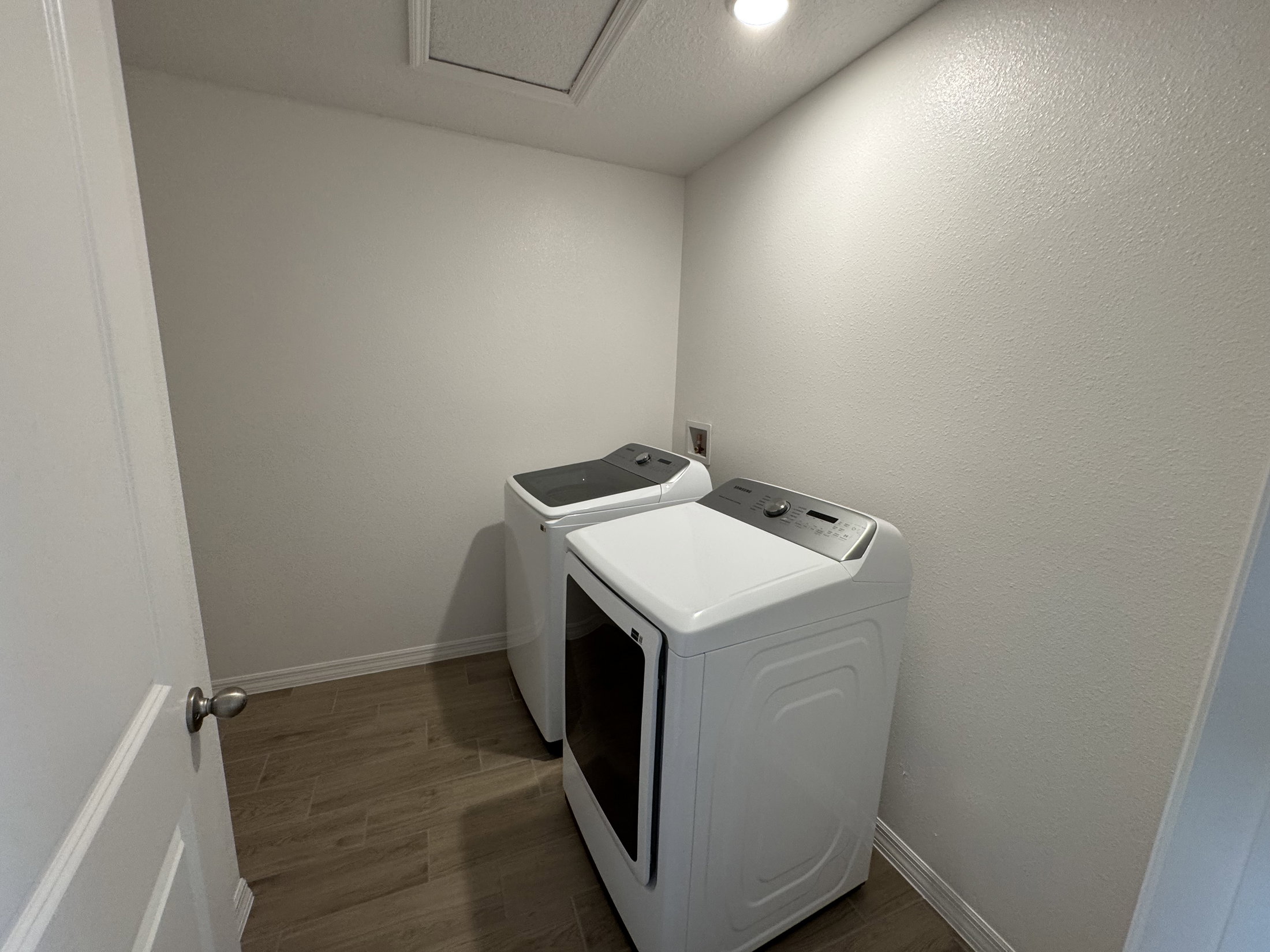 Two white laundry appliances in a small, well-lit laundry room with light-colored walls and wood flooring.