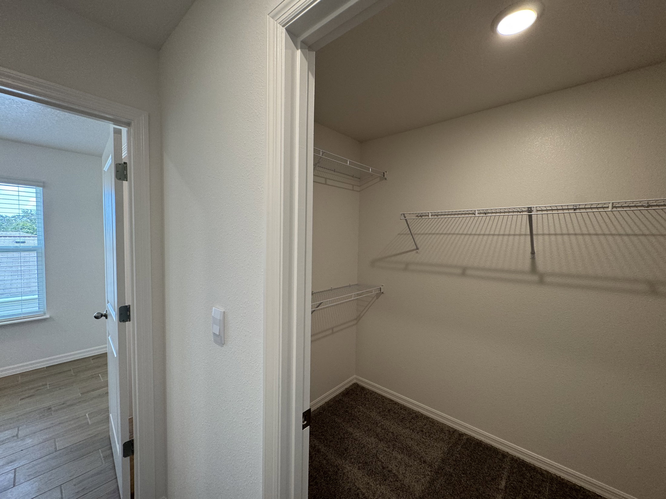 A brightly lit room with a closet featuring wire shelves and a door to another room.