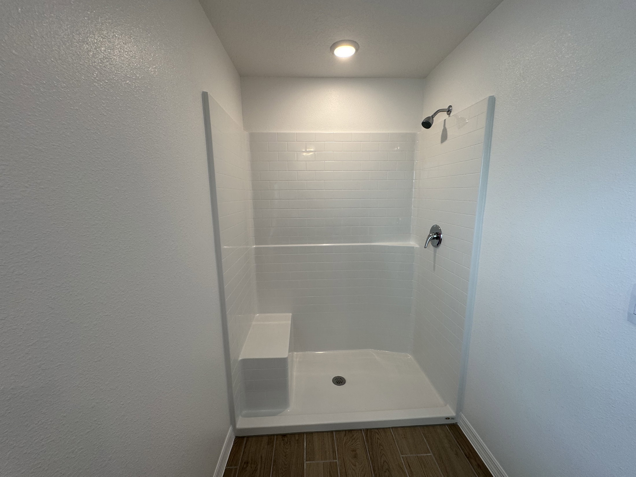 A modern, white tiled shower with a bench and showerhead against a plain white wall.