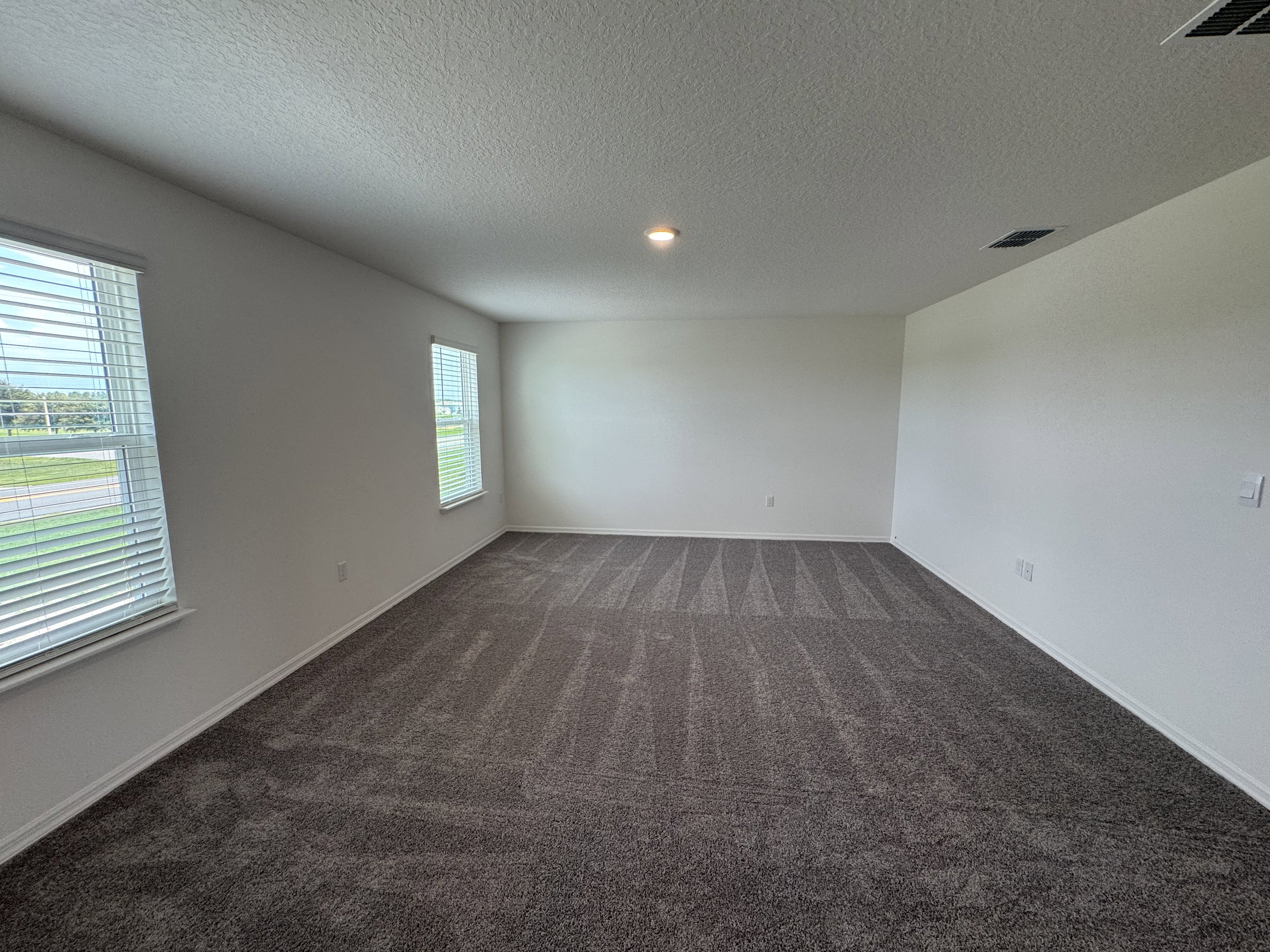 A newly carpeted, empty room with two windows and neutral-colored walls.