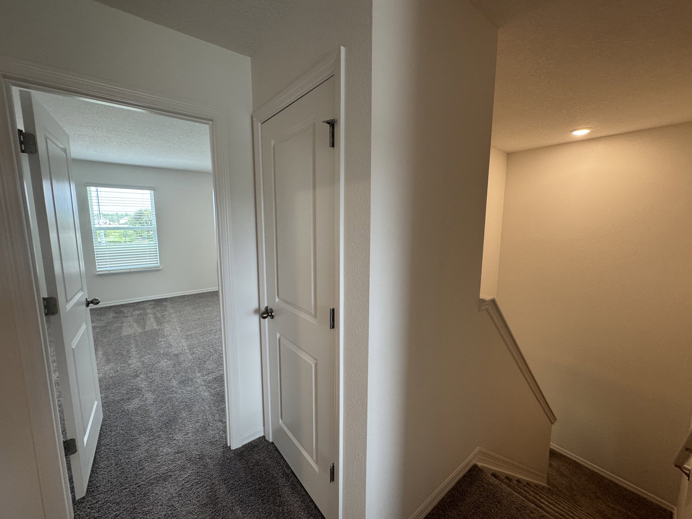 A hallway showing a door on the left, a staircase on the right, and a window at the far end.