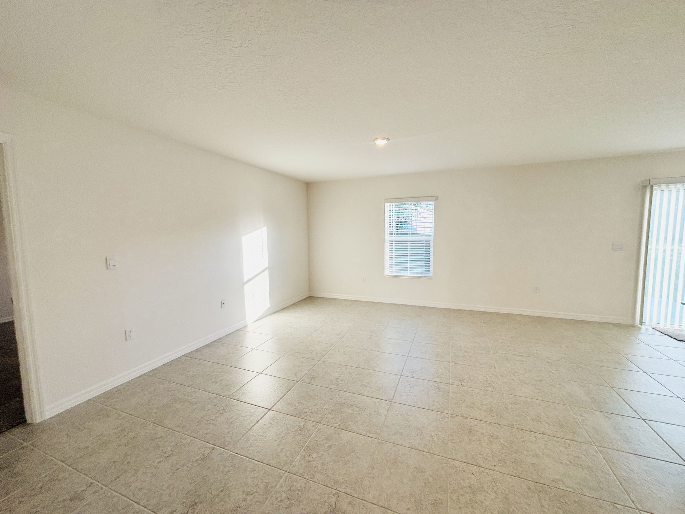Bright and spacious empty living room with large tile flooring and natural light streaming through the windows.