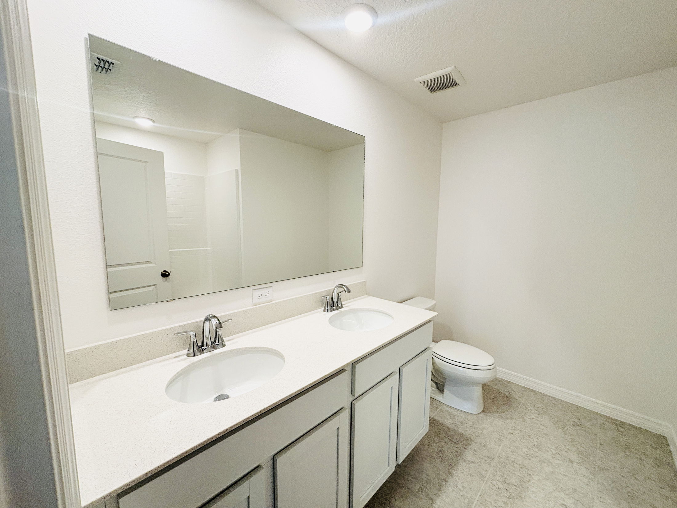 Modern bathroom featuring double sinks, a large mirror, and neutral-colored walls.