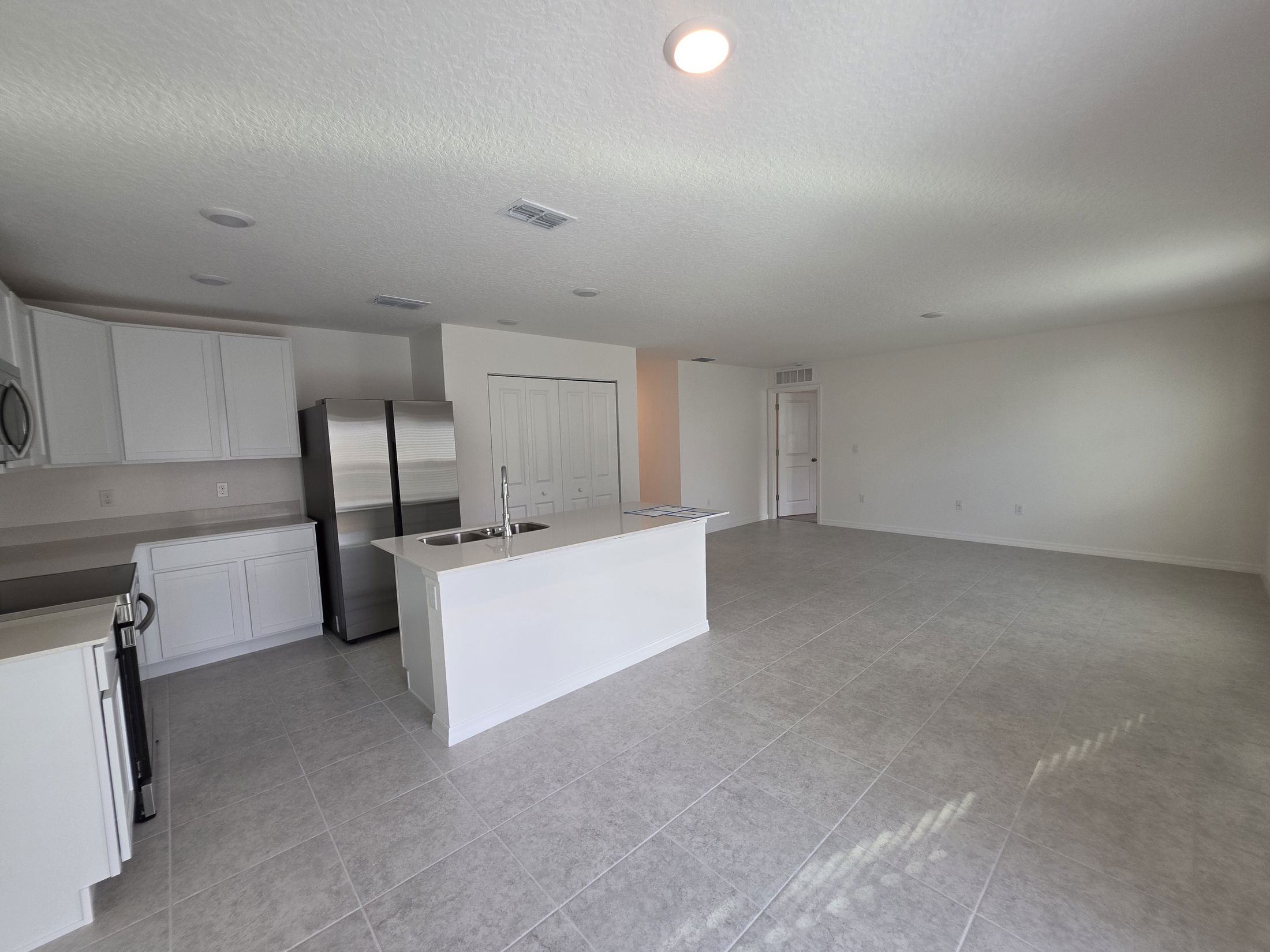 Spacious modern kitchen with stainless steel appliances and an open floor plan in a well-lit room featuring tile flooring.
