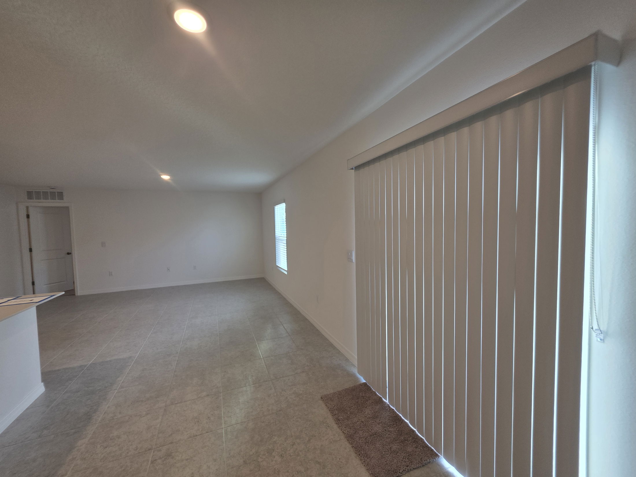 Spacious living room with neutral tile flooring and vertical blinds allowing natural light in.