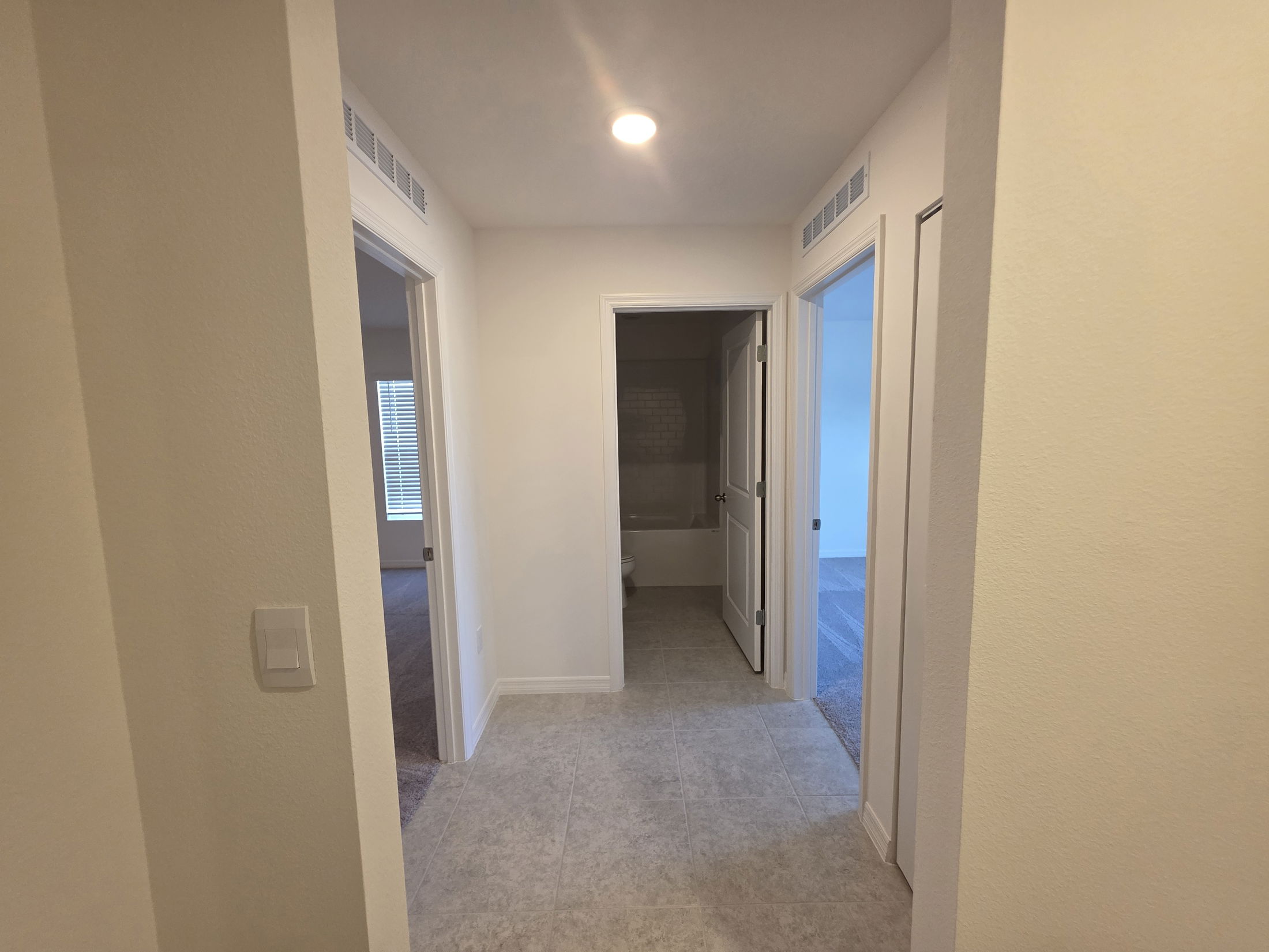 Modern apartment hallway with multiple doors leading to rooms, featuring neutral-colored walls and tiled flooring.