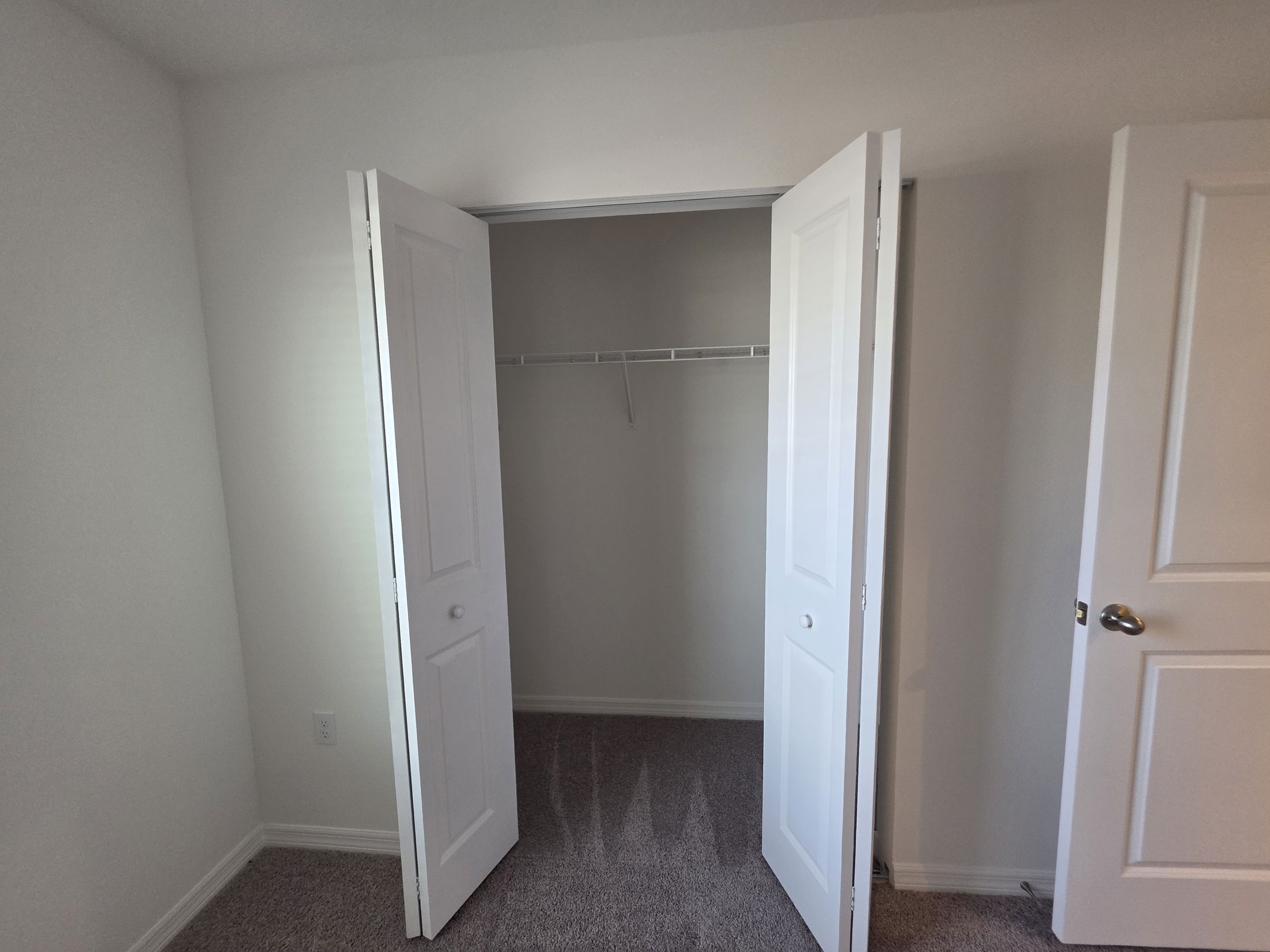 Empty closet with double doors in a clean, bright room featuring neutral walls and carpet.