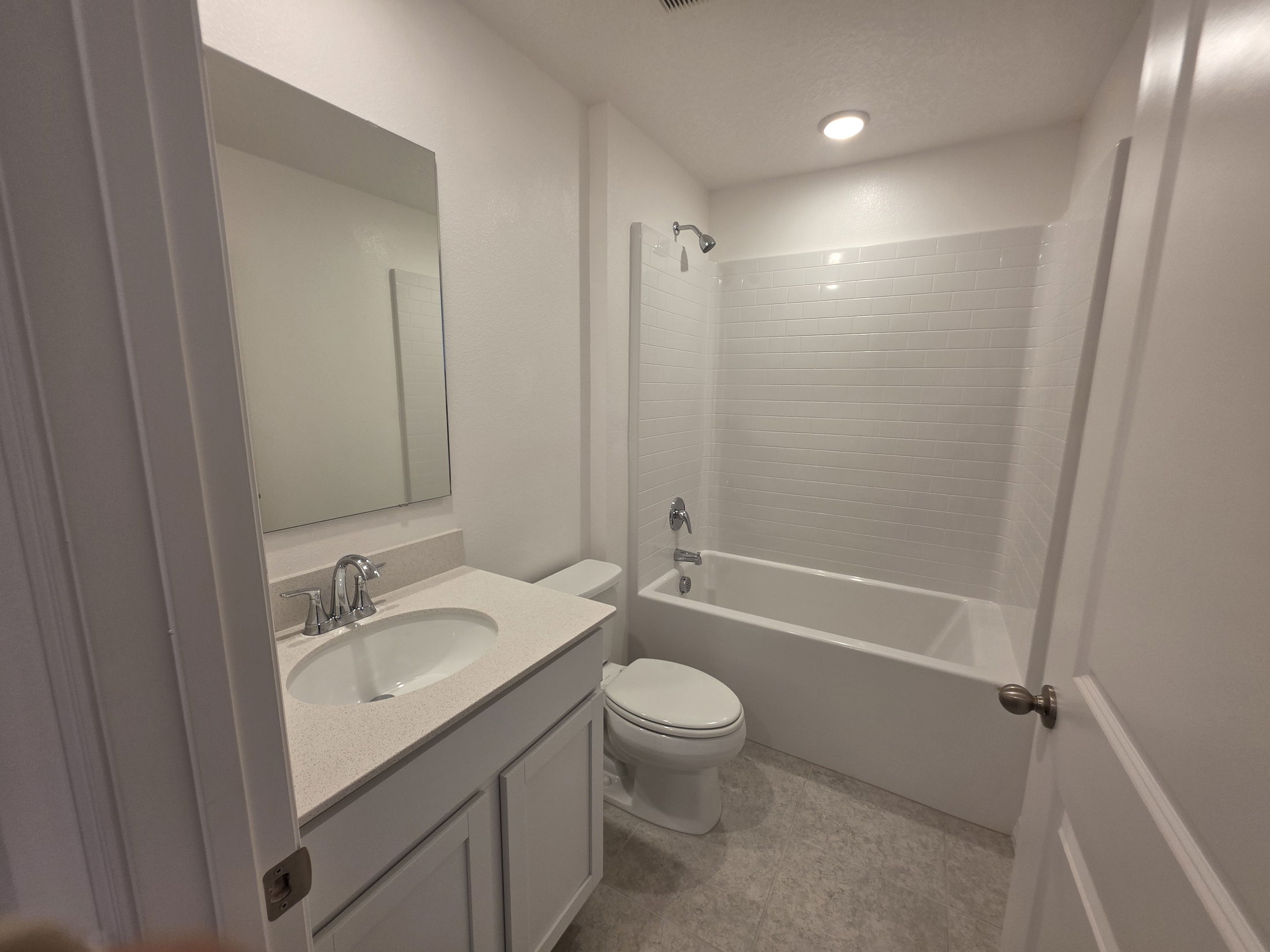 Modern bathroom featuring a white bathtub, shower, sink with mirror, and light-colored tile flooring.