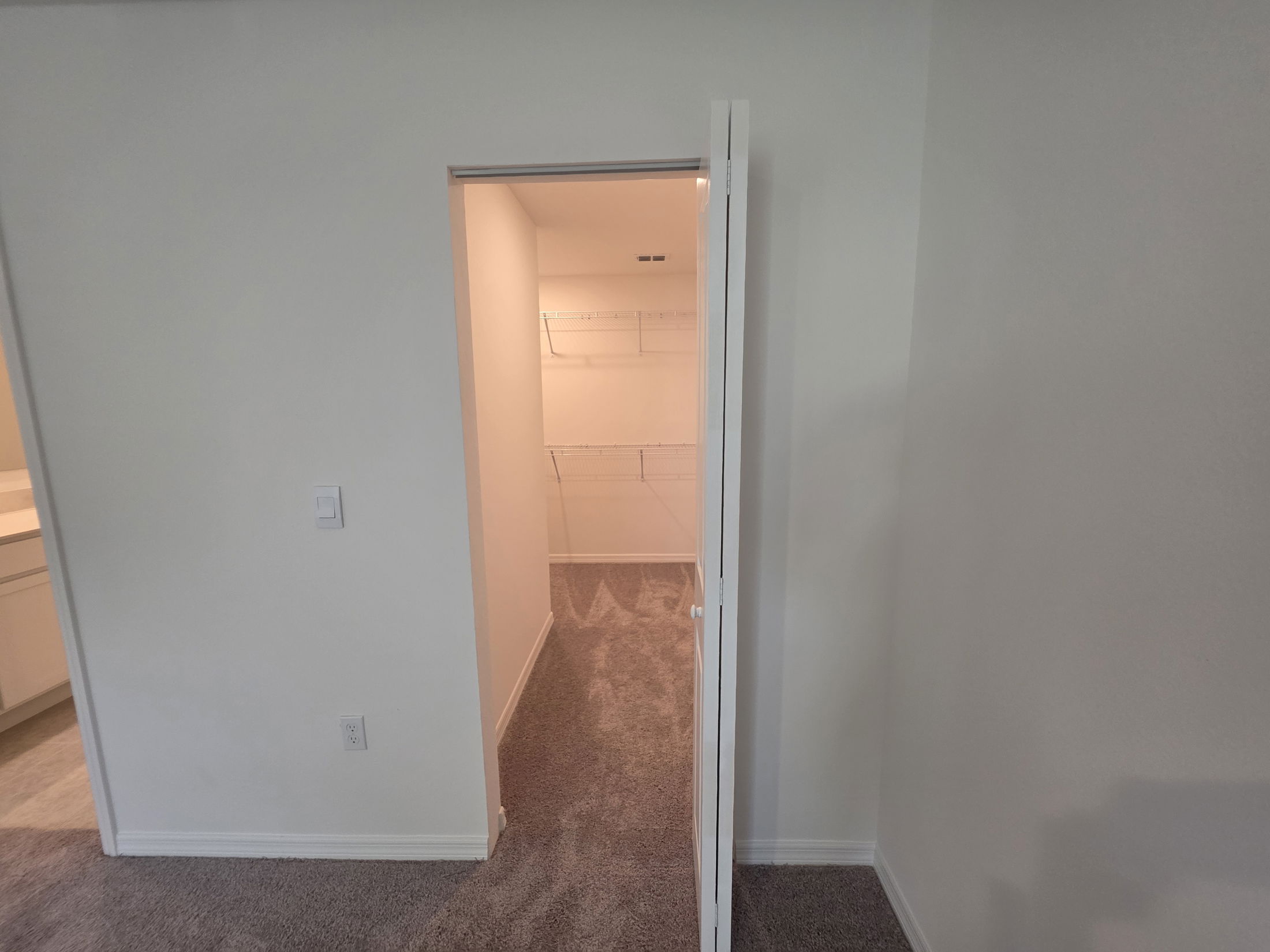Modern bedroom interior with a spacious walk-in closet view and plush carpet flooring.