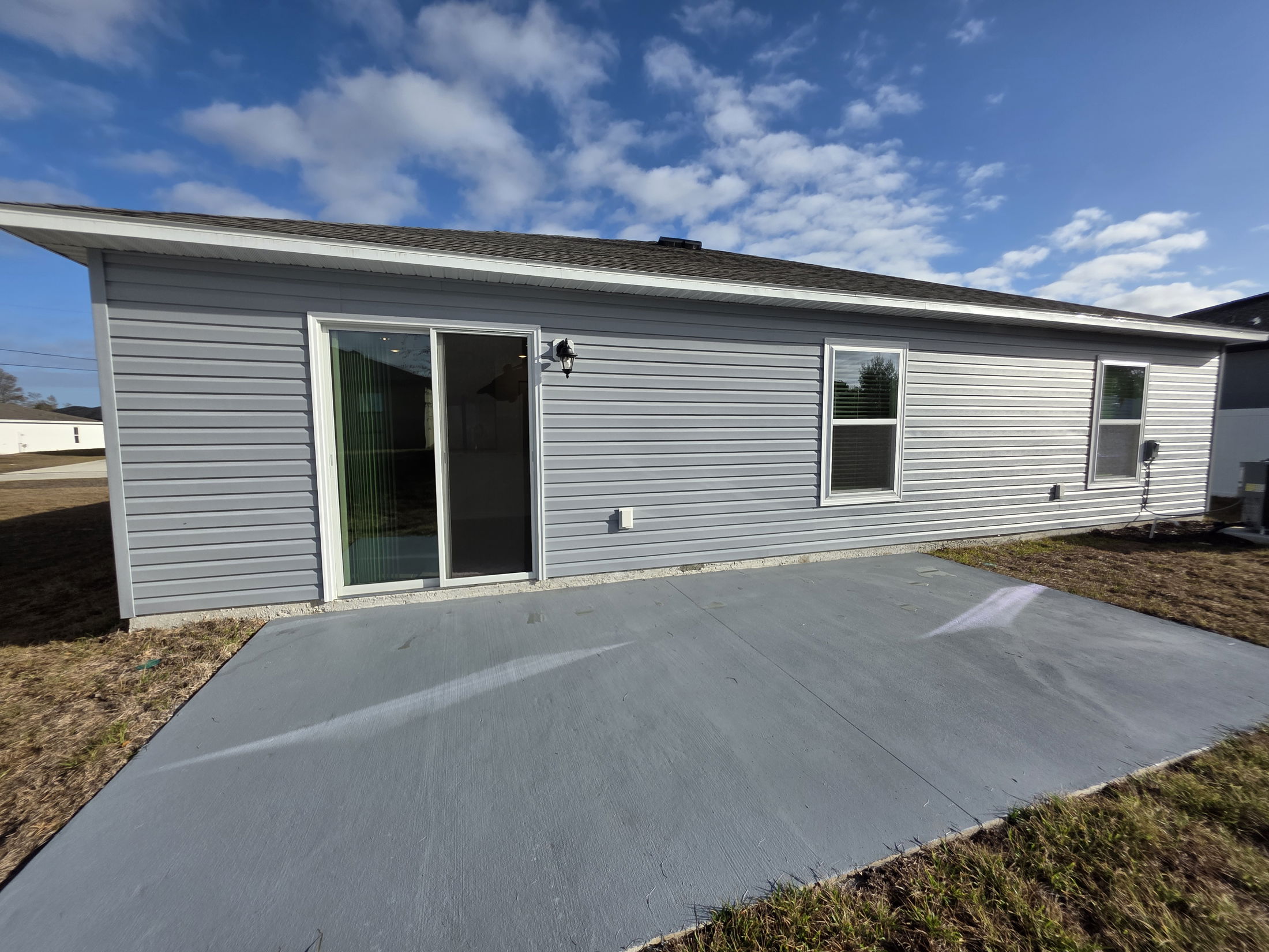 Exterior view of a modern gray house with sliding glass doors and a small patio, set against a clear blue sky.
