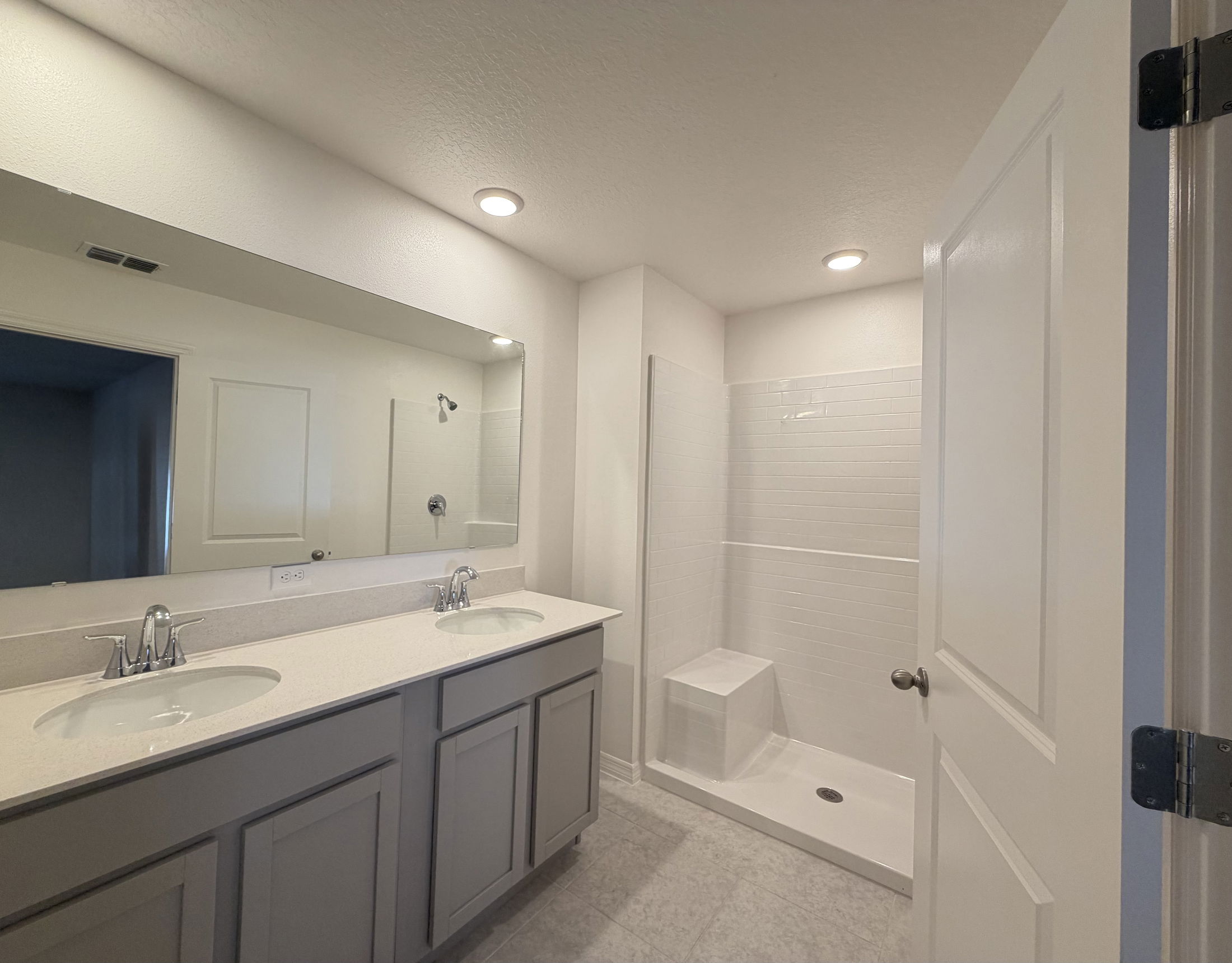 Modern bathroom with dual sinks, a large mirror, and a walk-in shower with a built-in bench.
