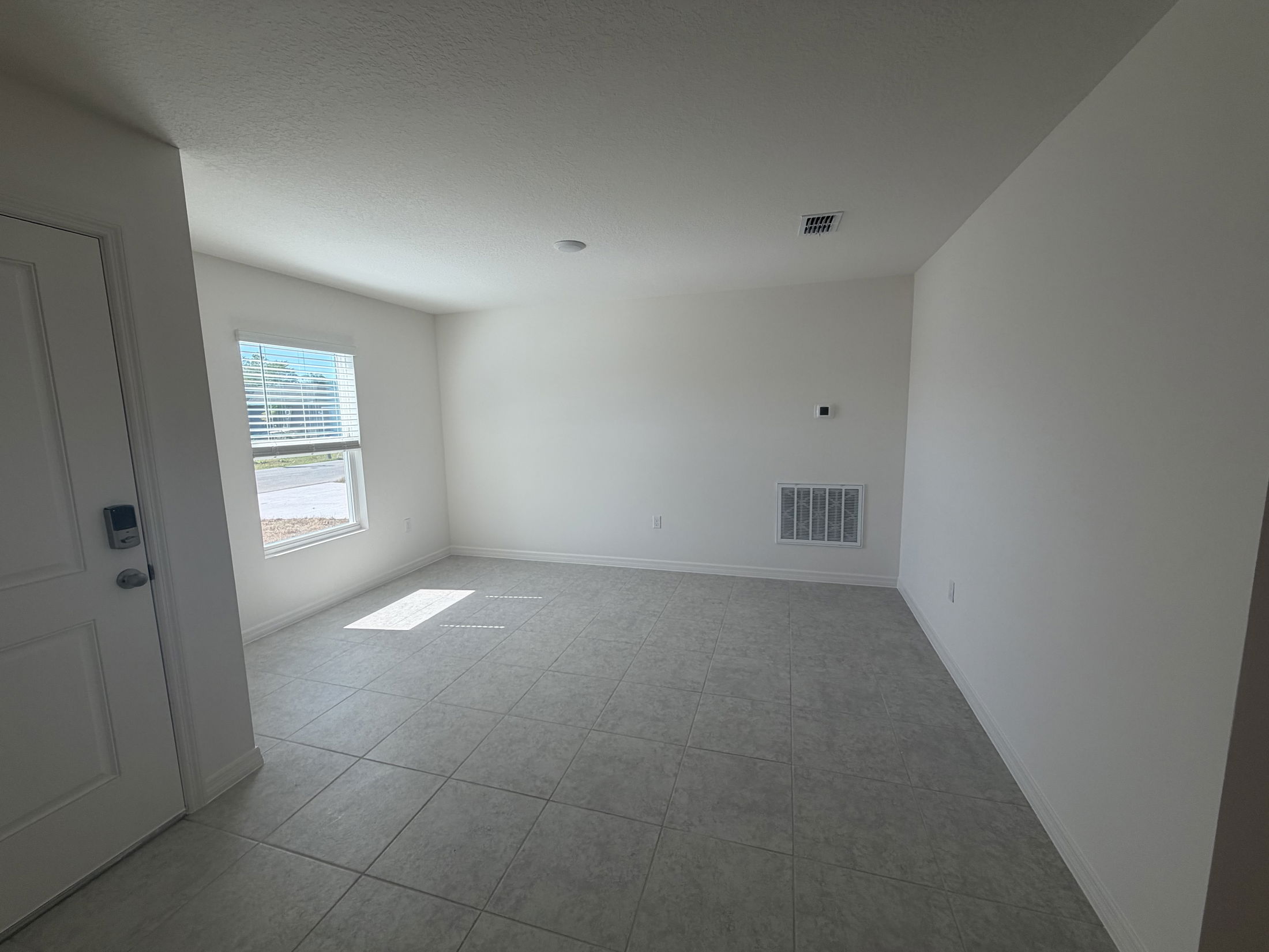 Bright, empty room with tiled flooring, white walls, a window, and a closed door.