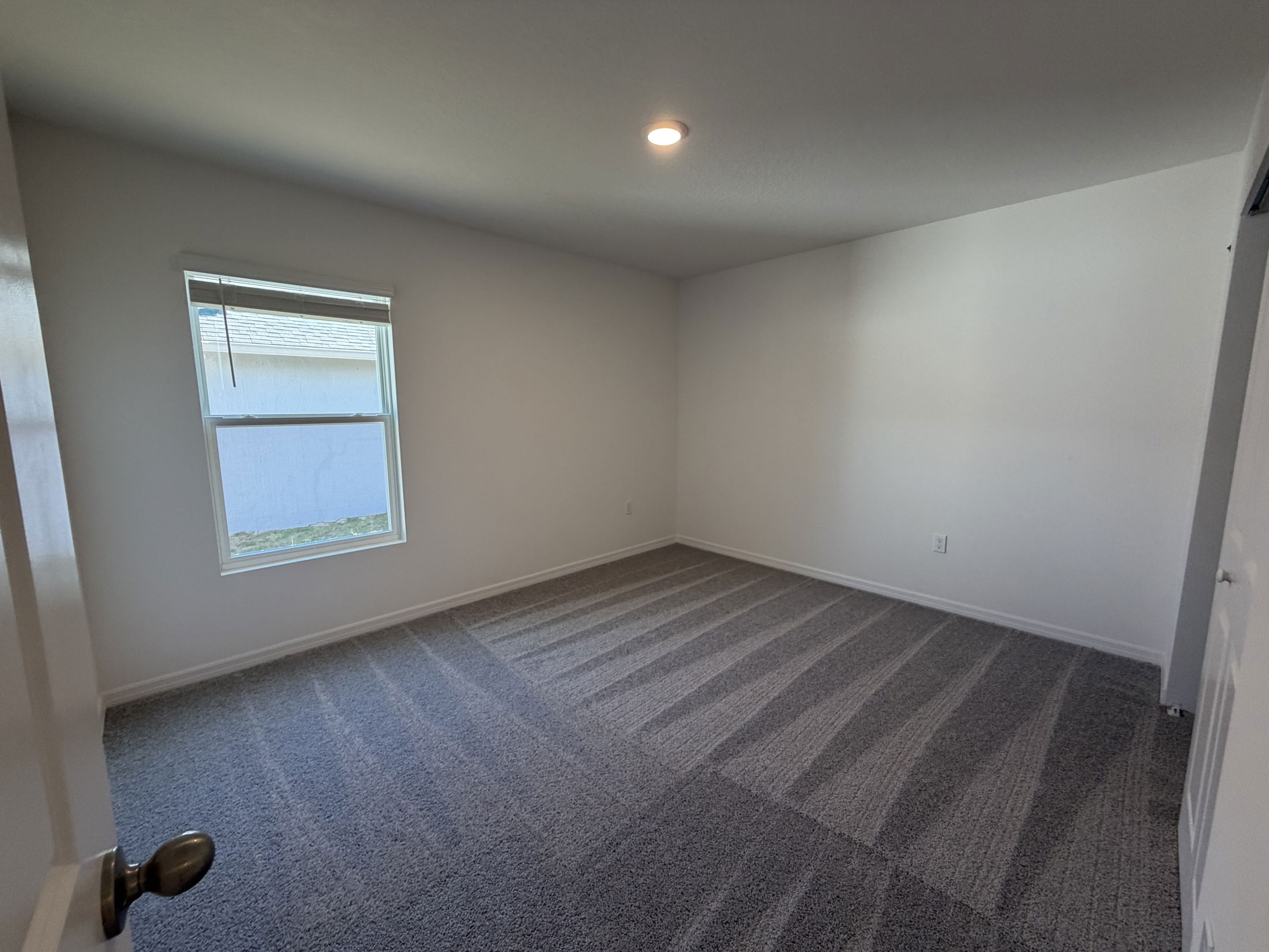Empty room with white walls, a single window, and freshly vacuumed carpet under soft lighting.