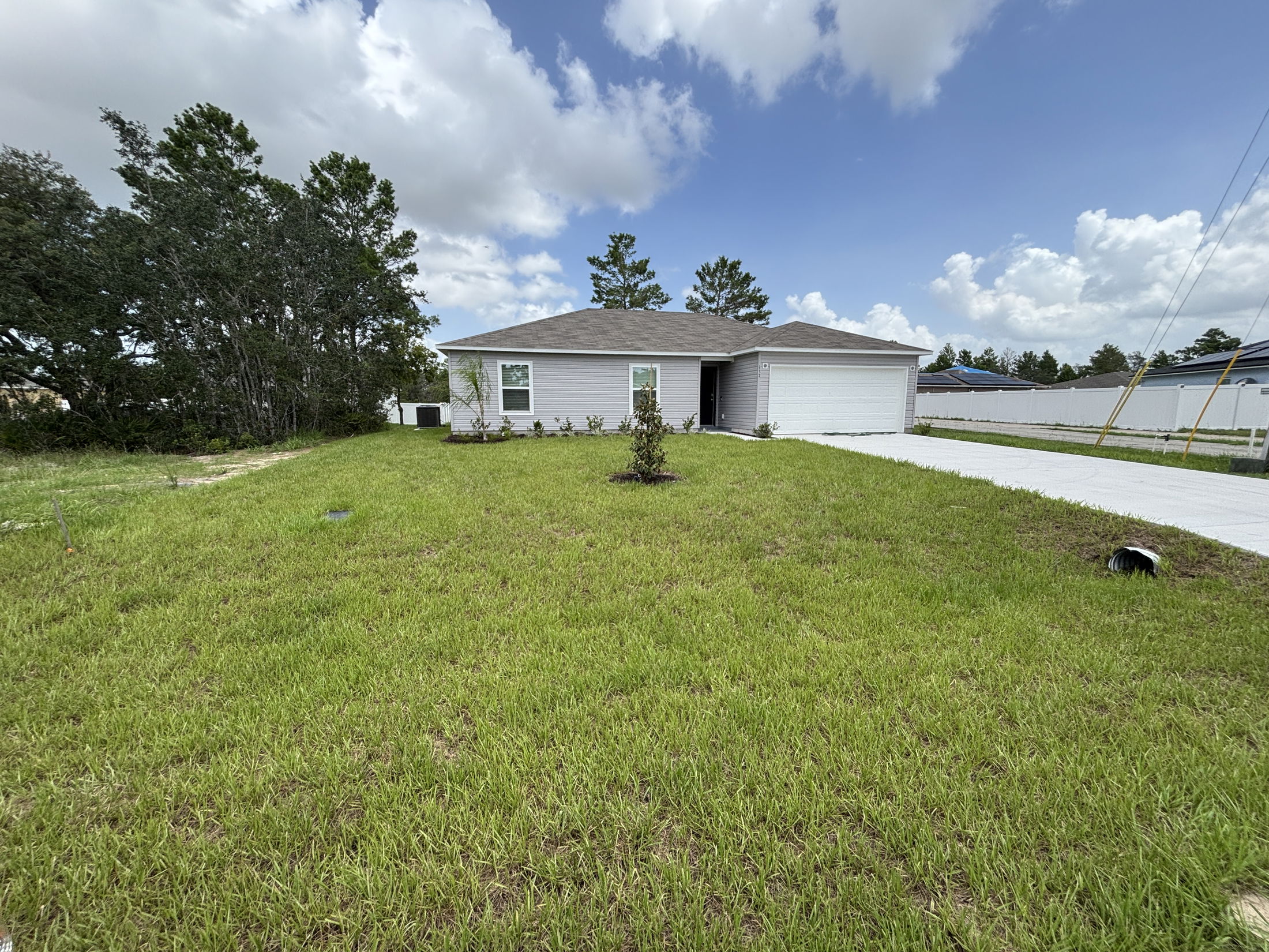 Single-story gray house with a two-car garage, large front lawn, and clear blue sky in a suburban neighborhood.
