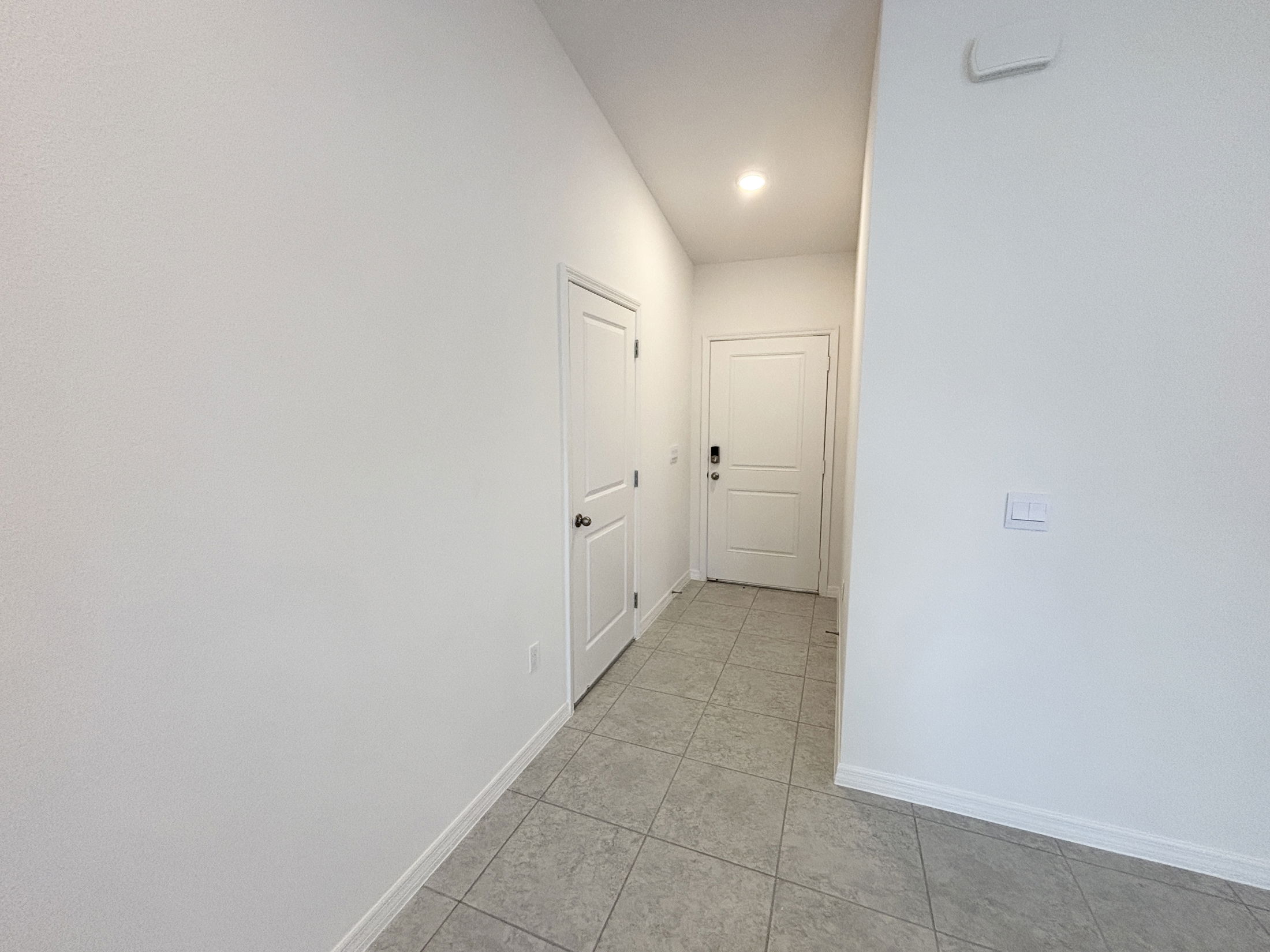 Minimalist white hallway interior with tile flooring and recessed lighting.