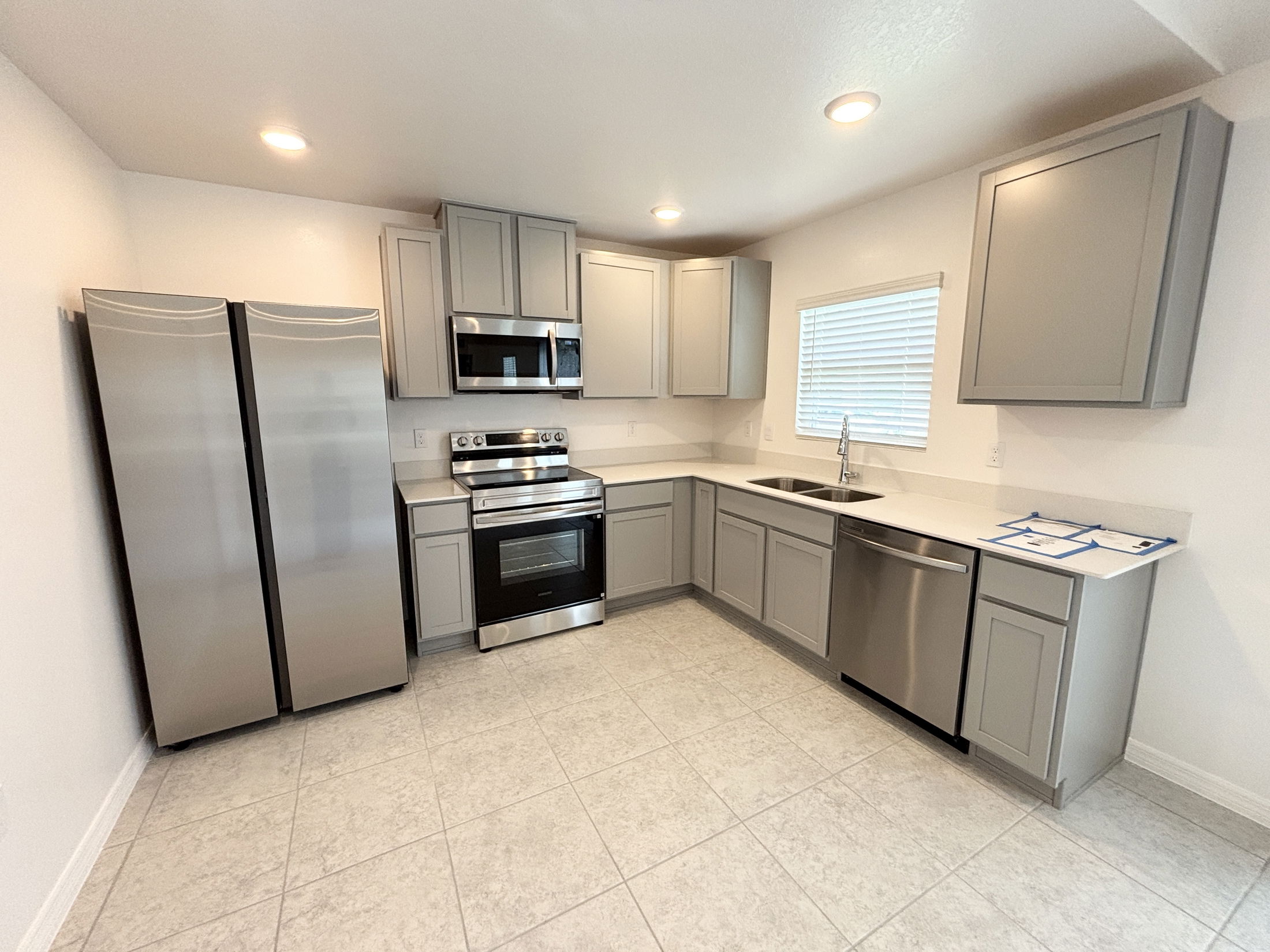 Modern kitchen with gray cabinets, stainless steel appliances, and tiled flooring.