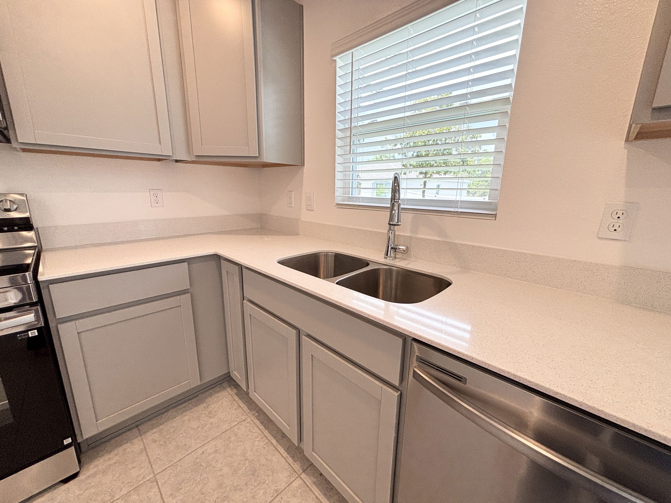Modern kitchen with light gray cabinets, stainless steel double sink, and large window.