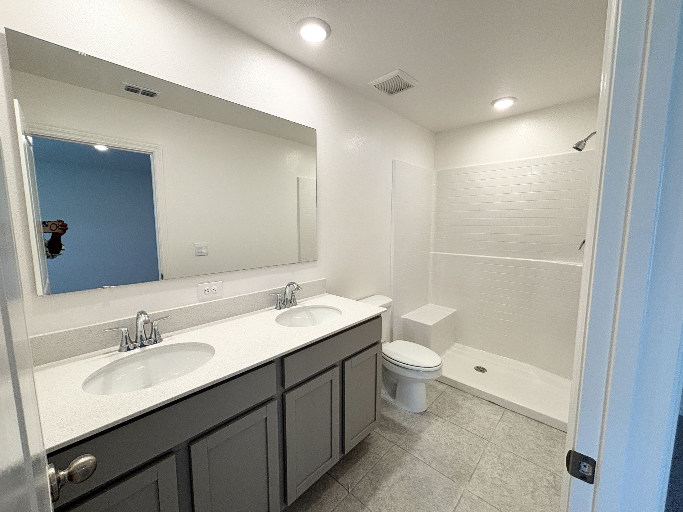 Modern bathroom featuring a spacious double vanity with sleek faucets, a large mirror, and a walk-in shower.