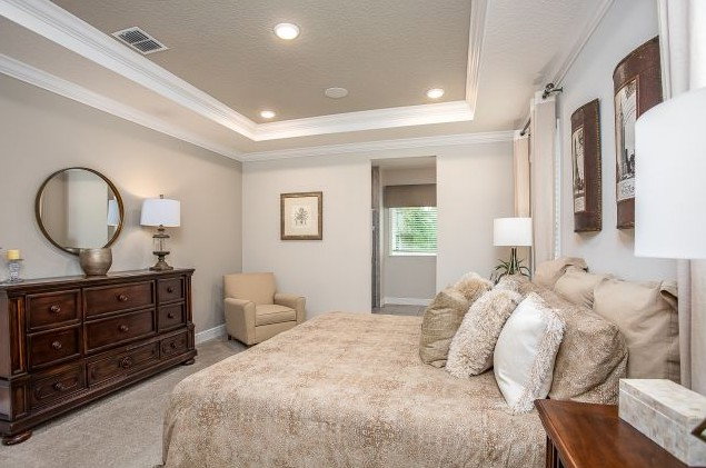 Cozy and elegant master bedroom featuring a queen-sized bed, decorative pillows, wooden dresser, and soft lighting in a neutral color palette.