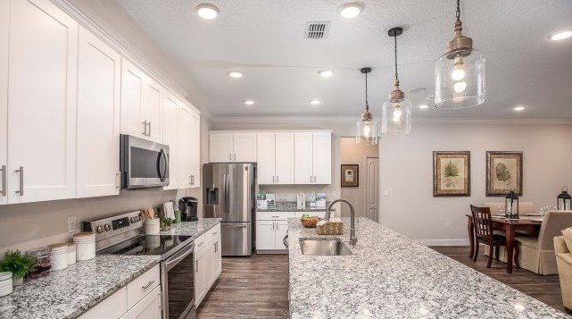 Modern kitchen featuring white cabinets, granite countertops, stainless steel appliances, and pendant lighting over a spacious island.