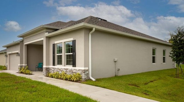 A modern gray house with stone accents and a neatly landscaped lawn under a cloudy sky.