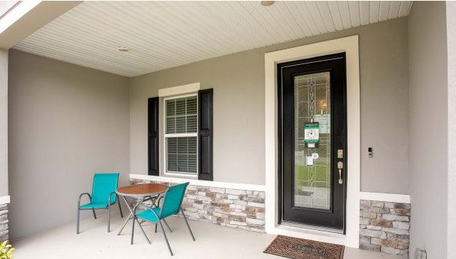 A cozy front porch featuring a circular table and two teal chairs beside a decorative stone accent wall and a modern black front door.