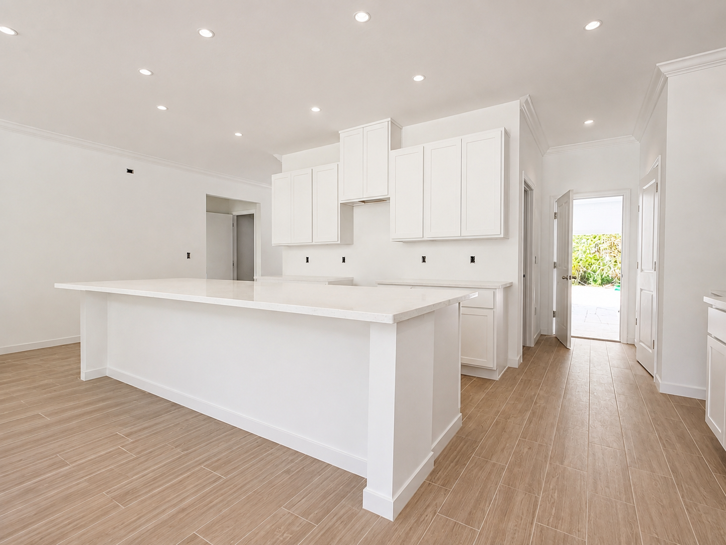 Bright, modern kitchen with white cabinetry and a large island, featuring warm wood flooring and an open doorway leading outside.