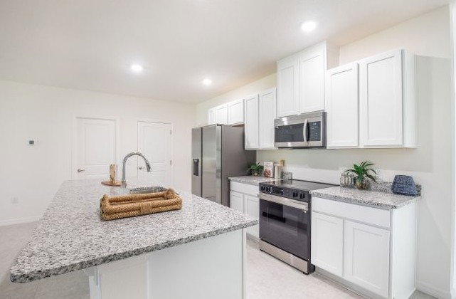 Modern kitchen featuring white cabinets, granite countertops, stainless steel appliances, and a large island with a wicker tray.
