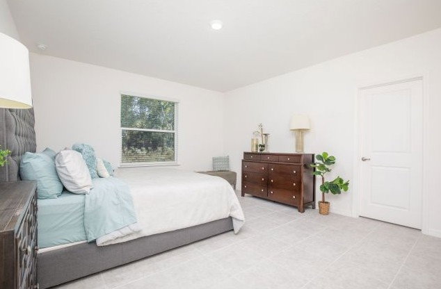 A neatly arranged bedroom featuring a bed with light blue linens, a wooden dresser, and a window allowing natural light.