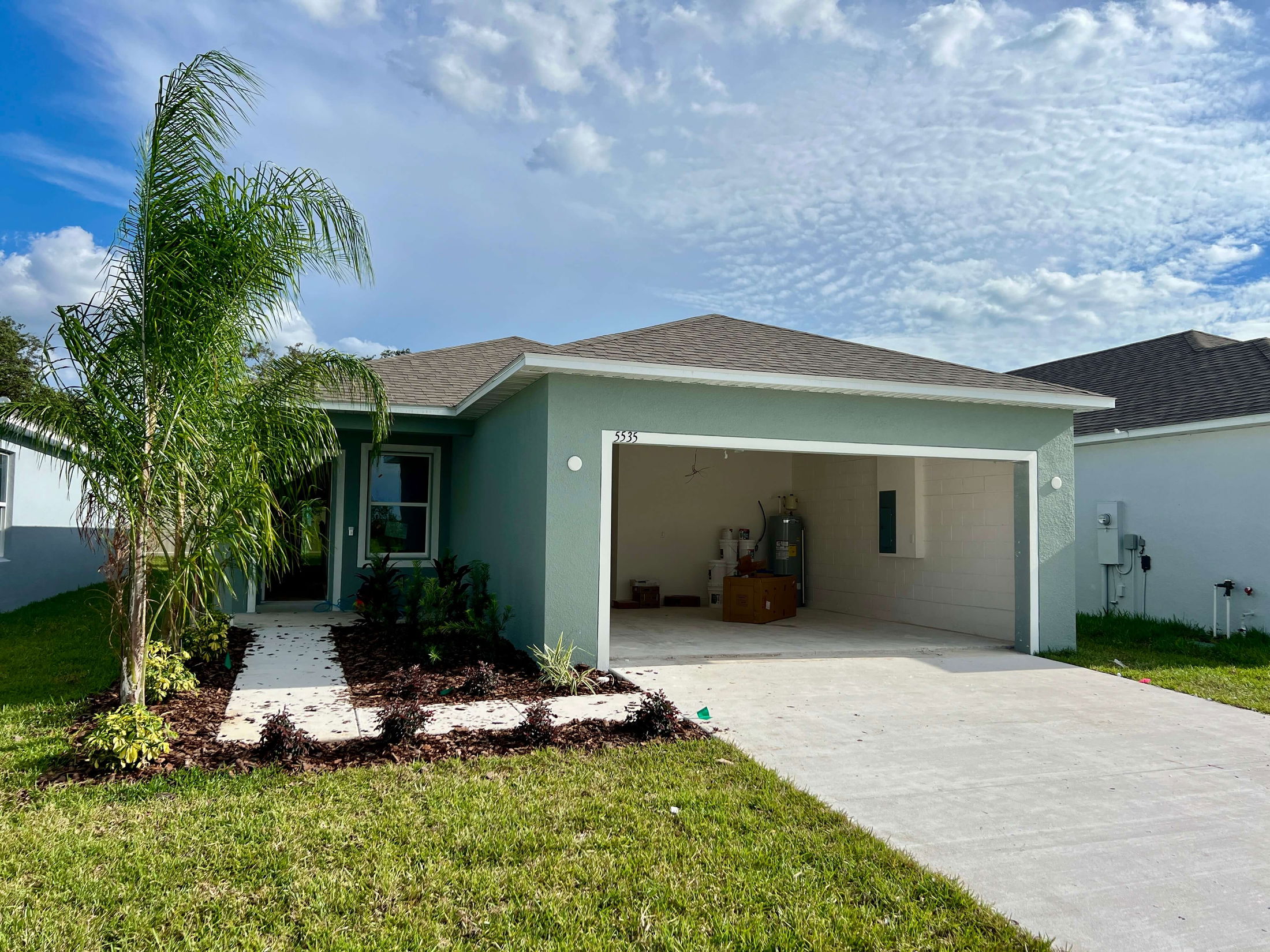 Modern suburban house with a two-car garage and landscaped front yard under a blue, cloudy sky.
