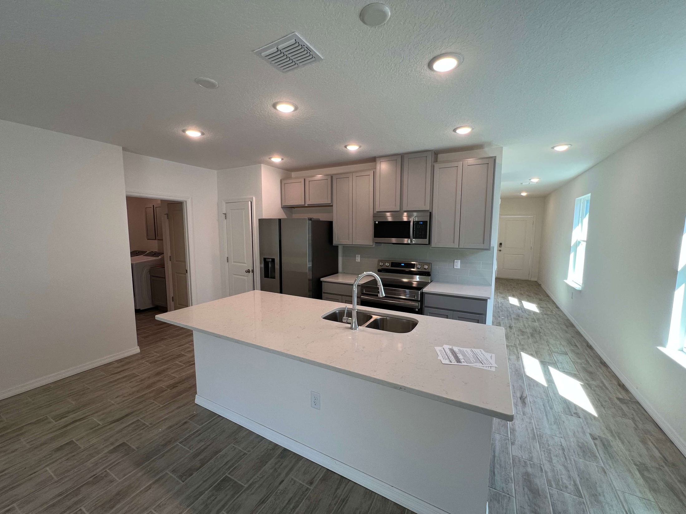 Modern kitchen with grey cabinets, stainless steel appliances, and a marble island in a bright open-concept layout.