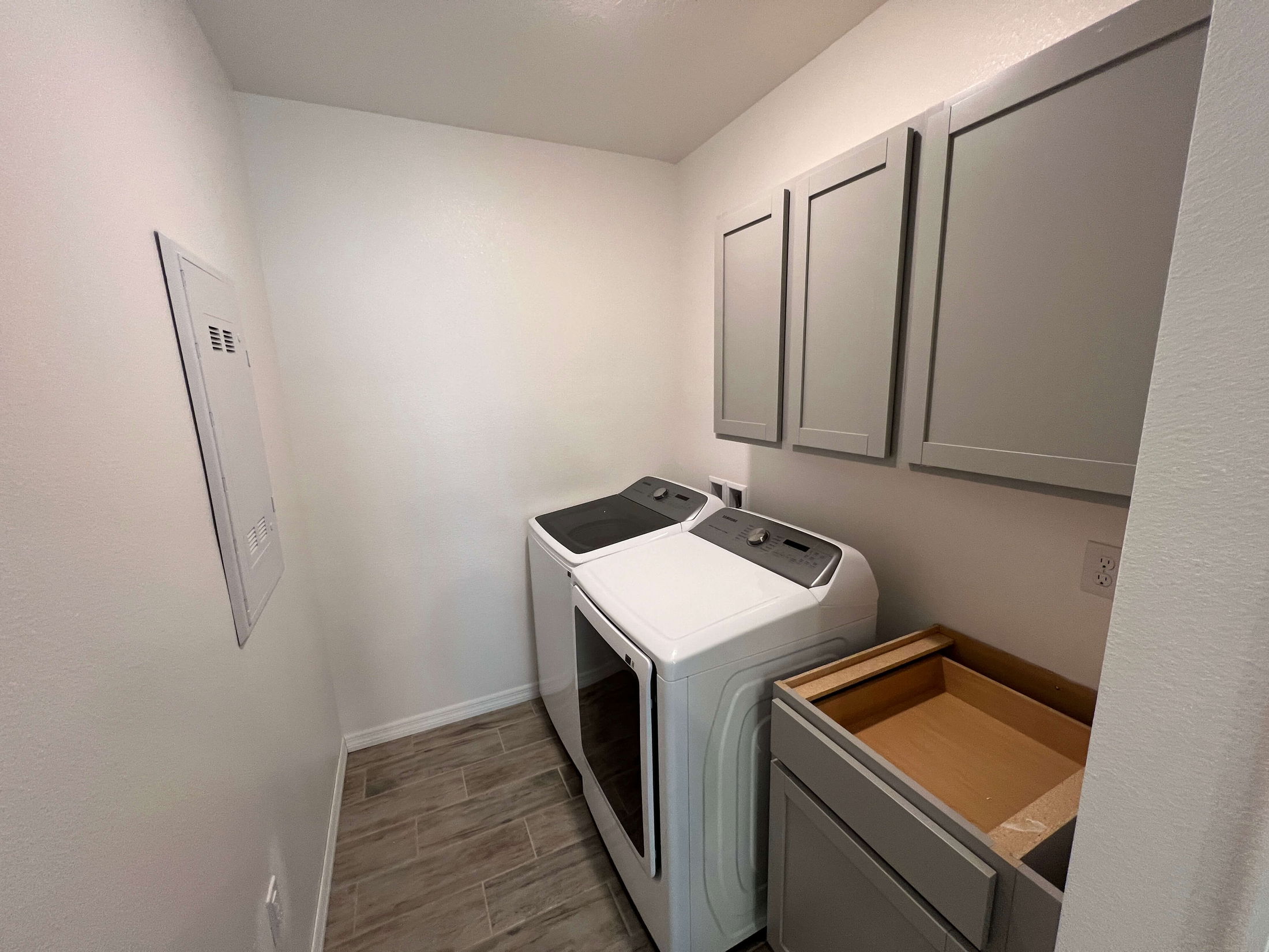 Modern laundry room with a washer and dryer, gray cabinets, and wood-look tile flooring.