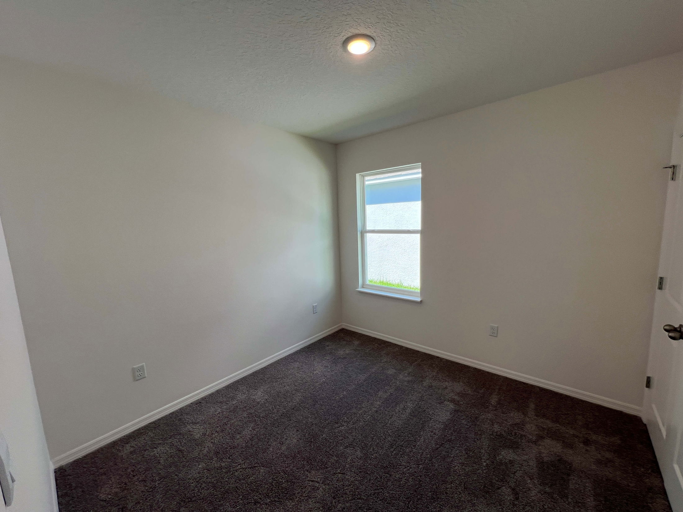 Empty room with white walls, a single window, and dark carpet flooring.