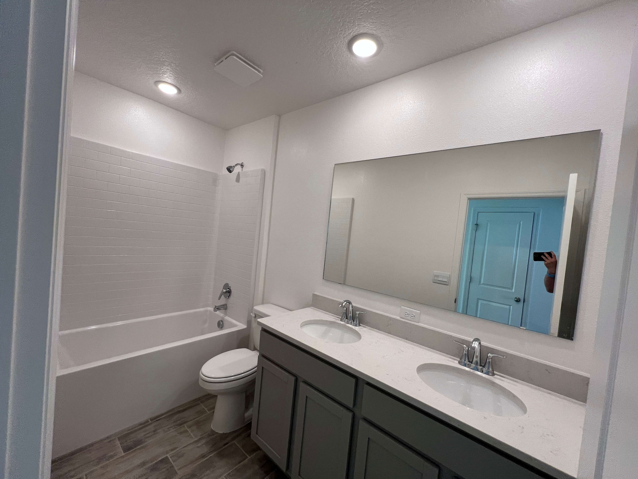 Modern bathroom with a double sink vanity, large mirror, and a bathtub with a tiled shower.