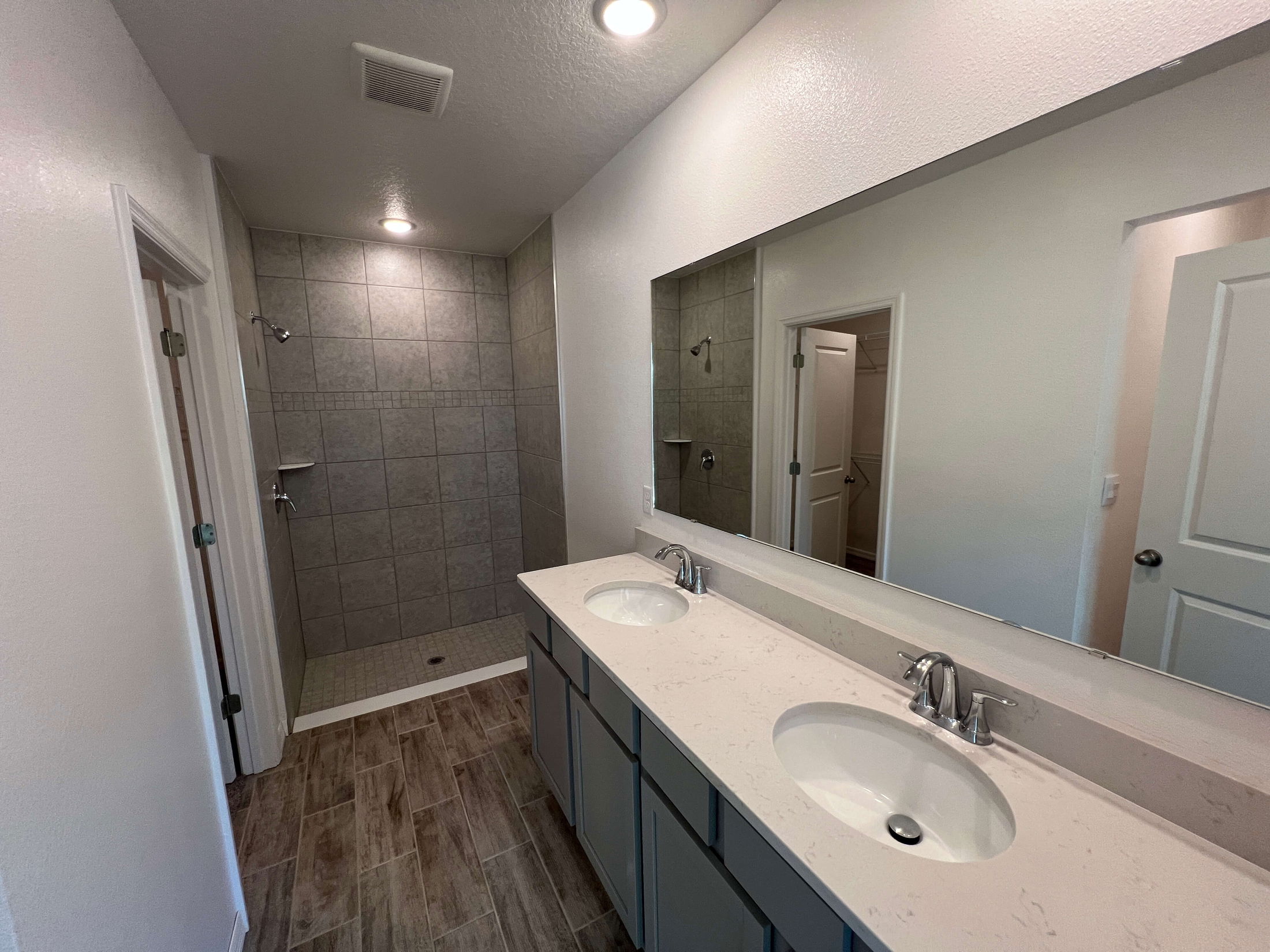 Modern bathroom with dual-sink vanity, large mirror, and tiled walk-in shower.