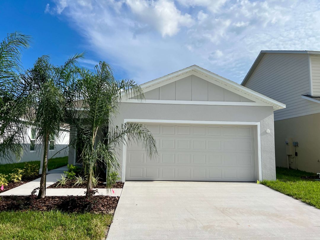 Modern single-family home with a two-car garage and palm tree landscaping under a clear blue sky.