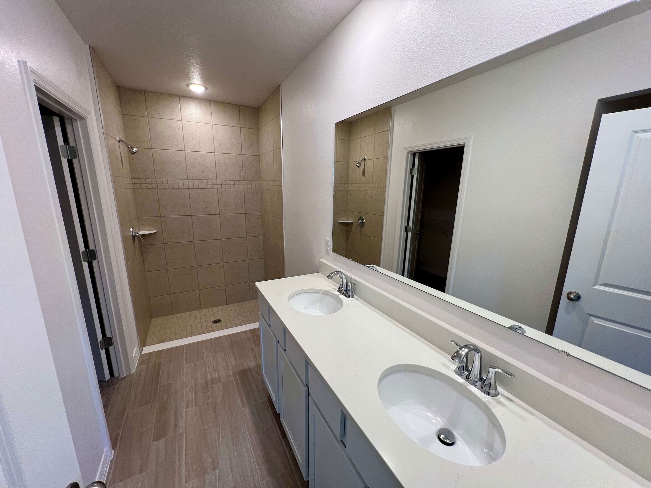 Modern bathroom with dual sinks, large mirror, and walk-in tiled shower.