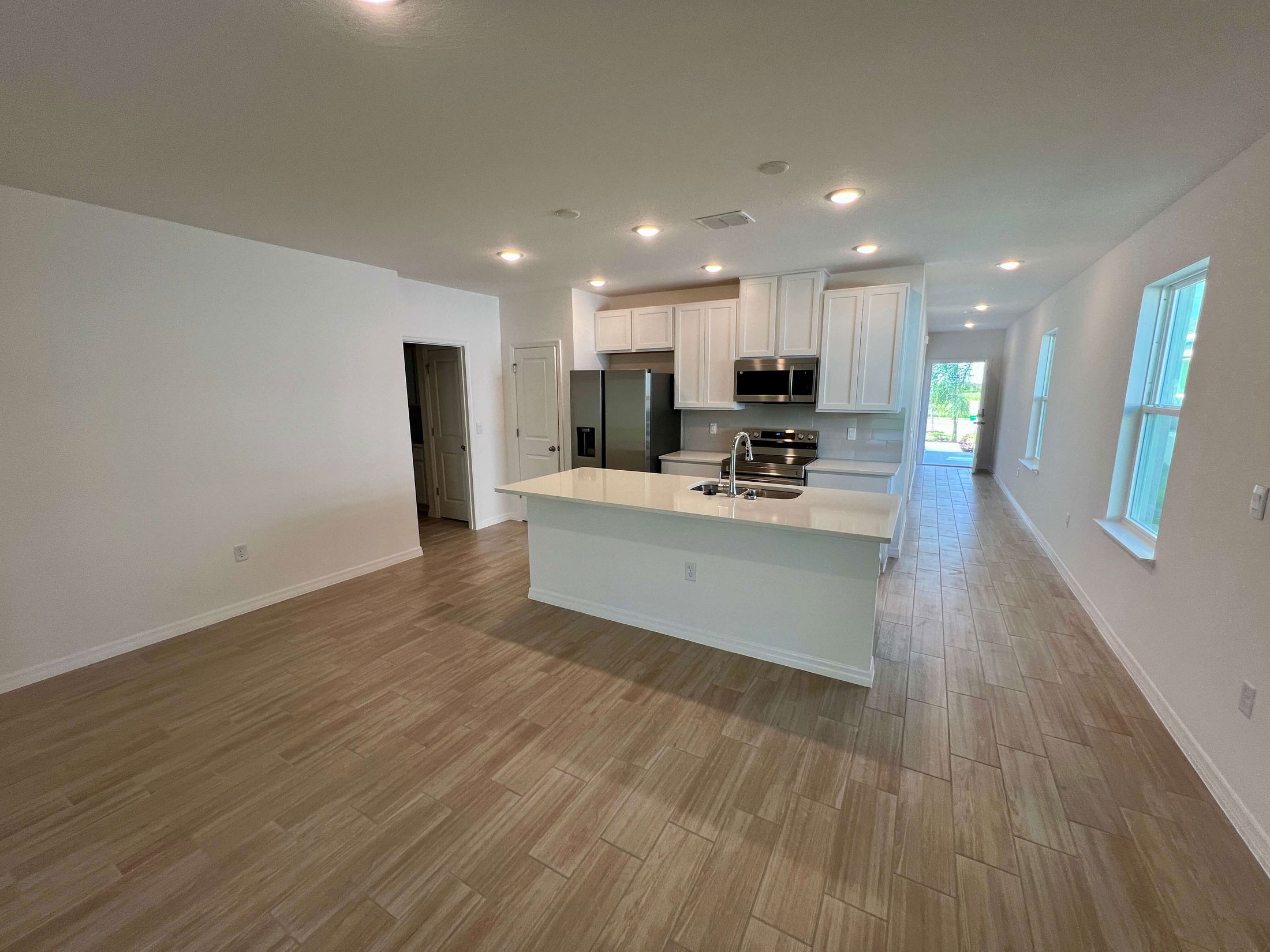 Modern, open-plan kitchen and living area with wood-look tile flooring and natural light from large windows.