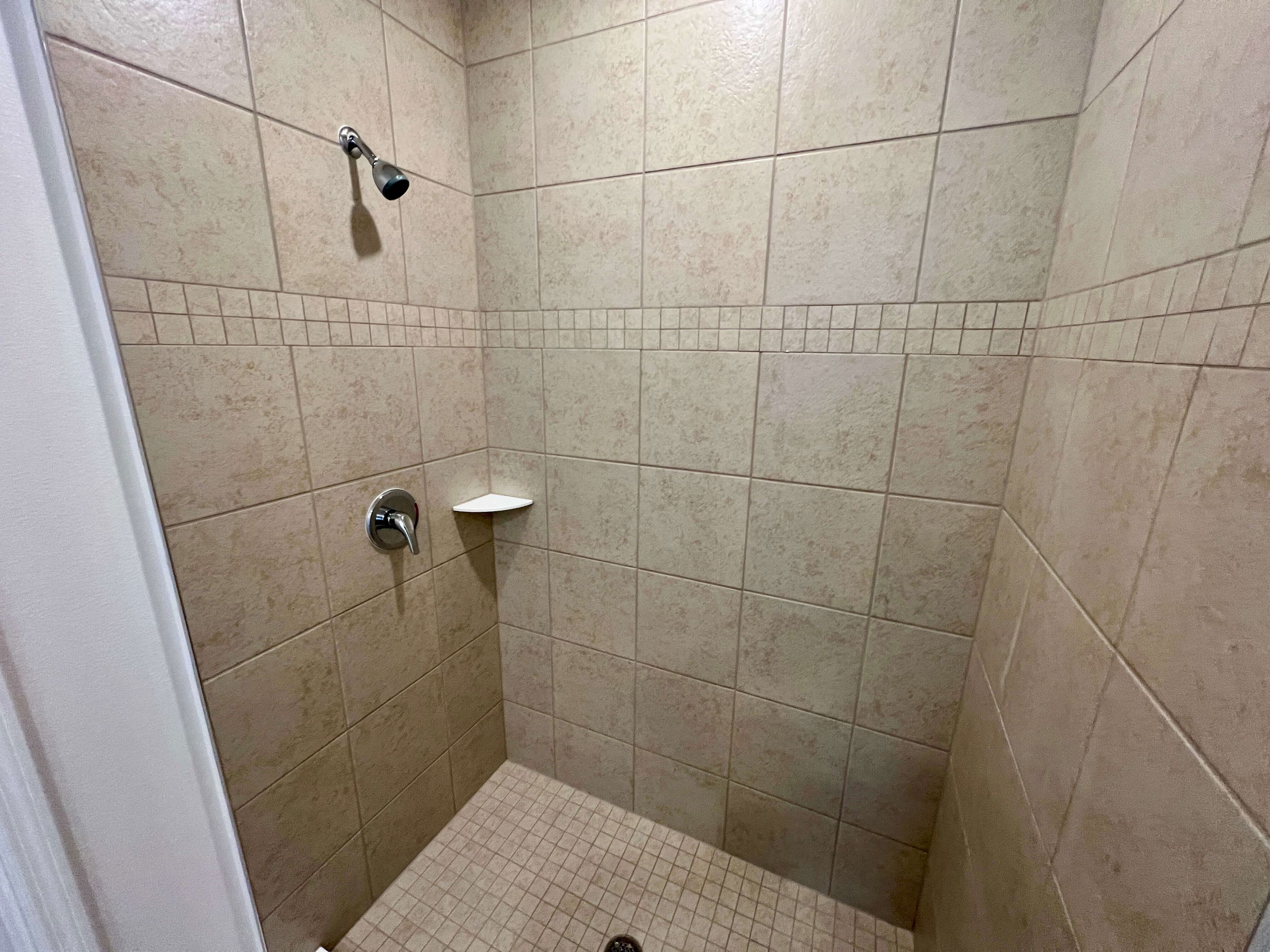 Tile shower corner with beige ceramic tiles, a modern showerhead, and a built-in soap shelf.