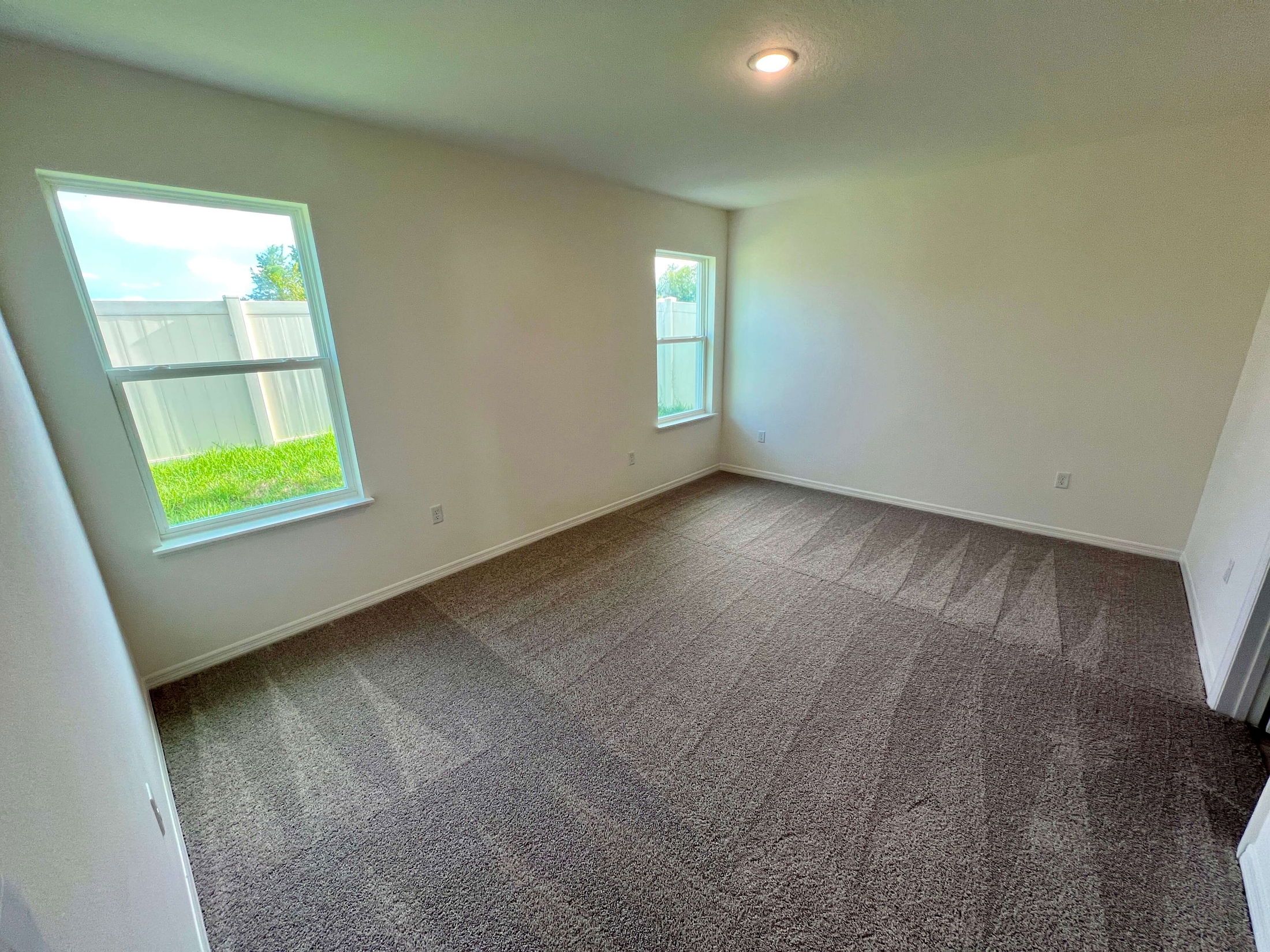 Spacious, freshly carpeted empty room with two windows allowing natural light.