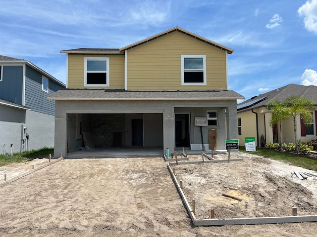 Two-story yellow house under construction with unfinished driveway in a residential neighborhood.