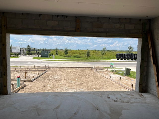 View of a construction site with a concrete foundation and a scenic background of a road and grassy landscape.