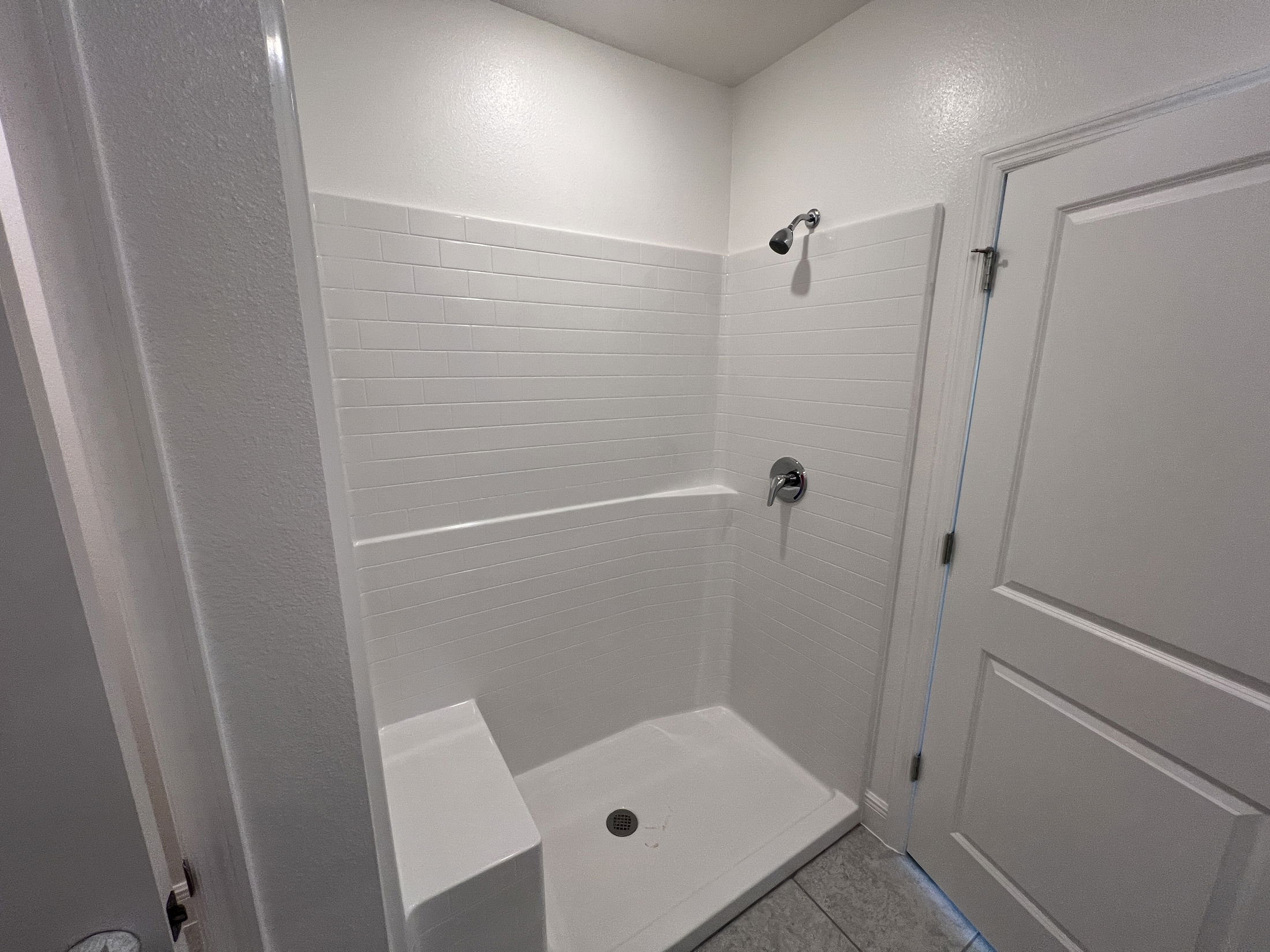 Minimalist white shower with a tiled interior, featuring a single showerhead and built-in bench in a modern bathroom.