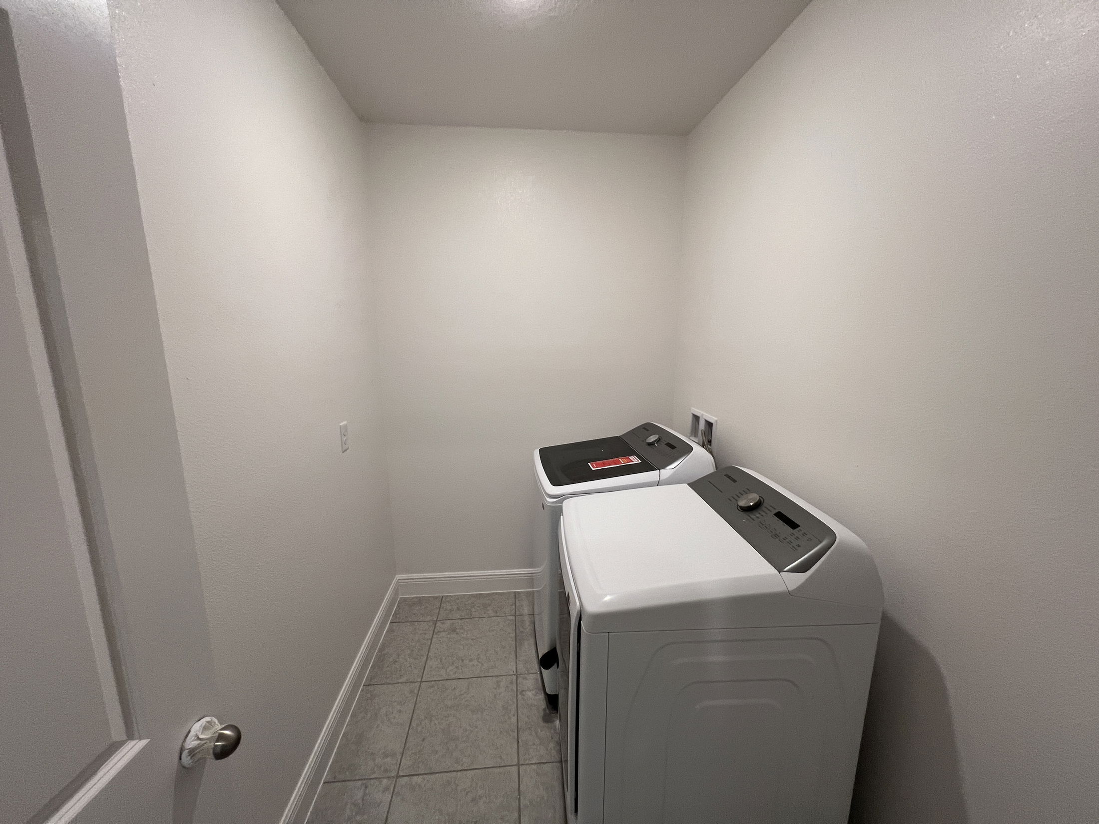 Compact laundry room with two modern white top-loading washing machines and gray tiled flooring.