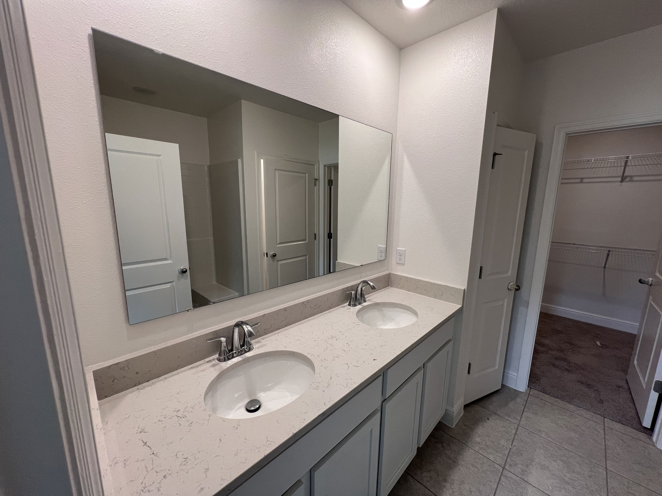 Modern bathroom with a double sink vanity, large mirror, and adjacent closet.