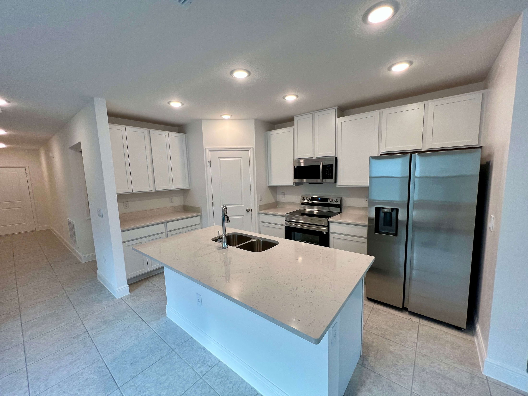 Modern kitchen with white cabinets, stainless steel appliances, and a central island with sink and quartz countertop.