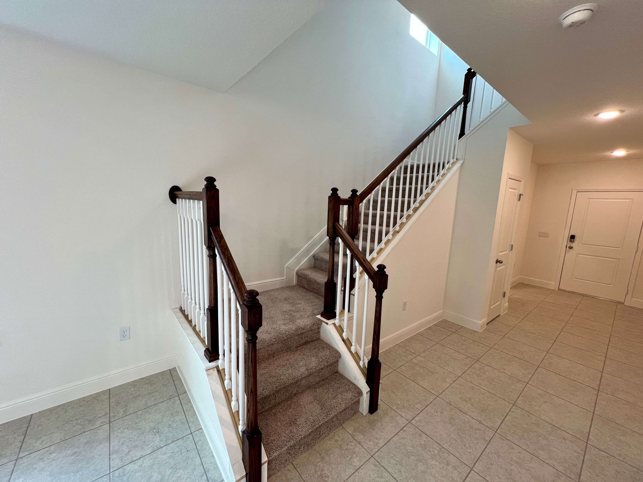 Spacious, modern entryway featuring a carpeted staircase with wooden banister and white spindles adjacent to a tiled floor.