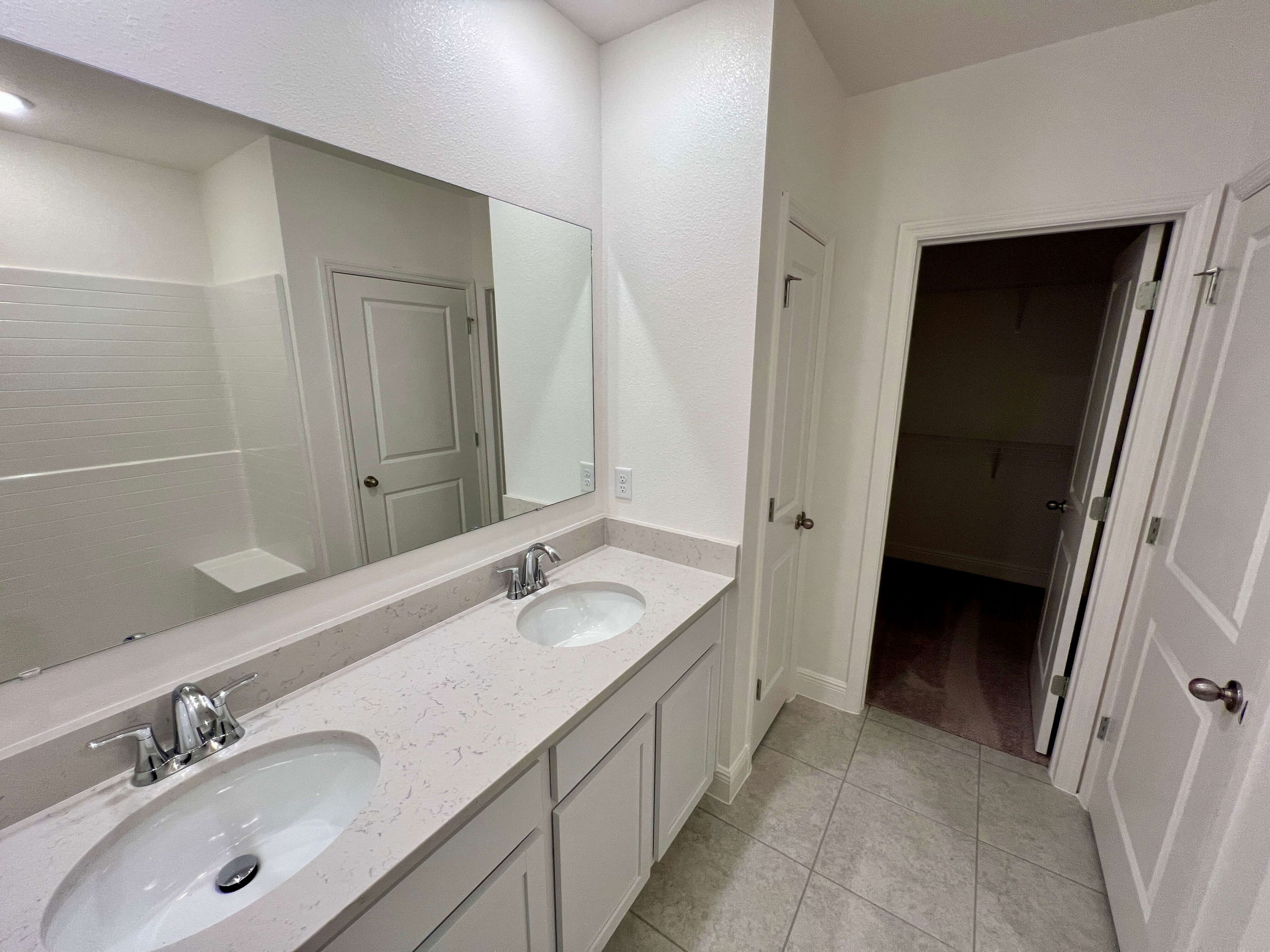 Modern bathroom featuring a double sink vanity with a large mirror, tiled flooring, and adjacent white doors.